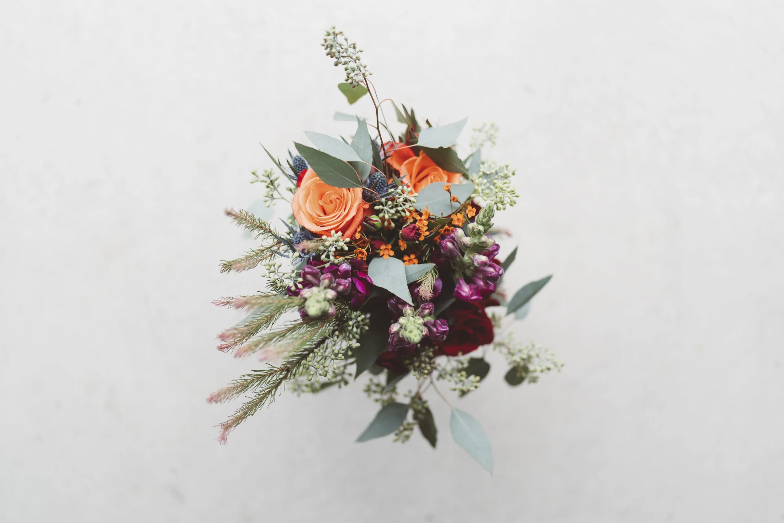 Colorful bouquet of orange roses, purple flowers, and greenery on a white background.