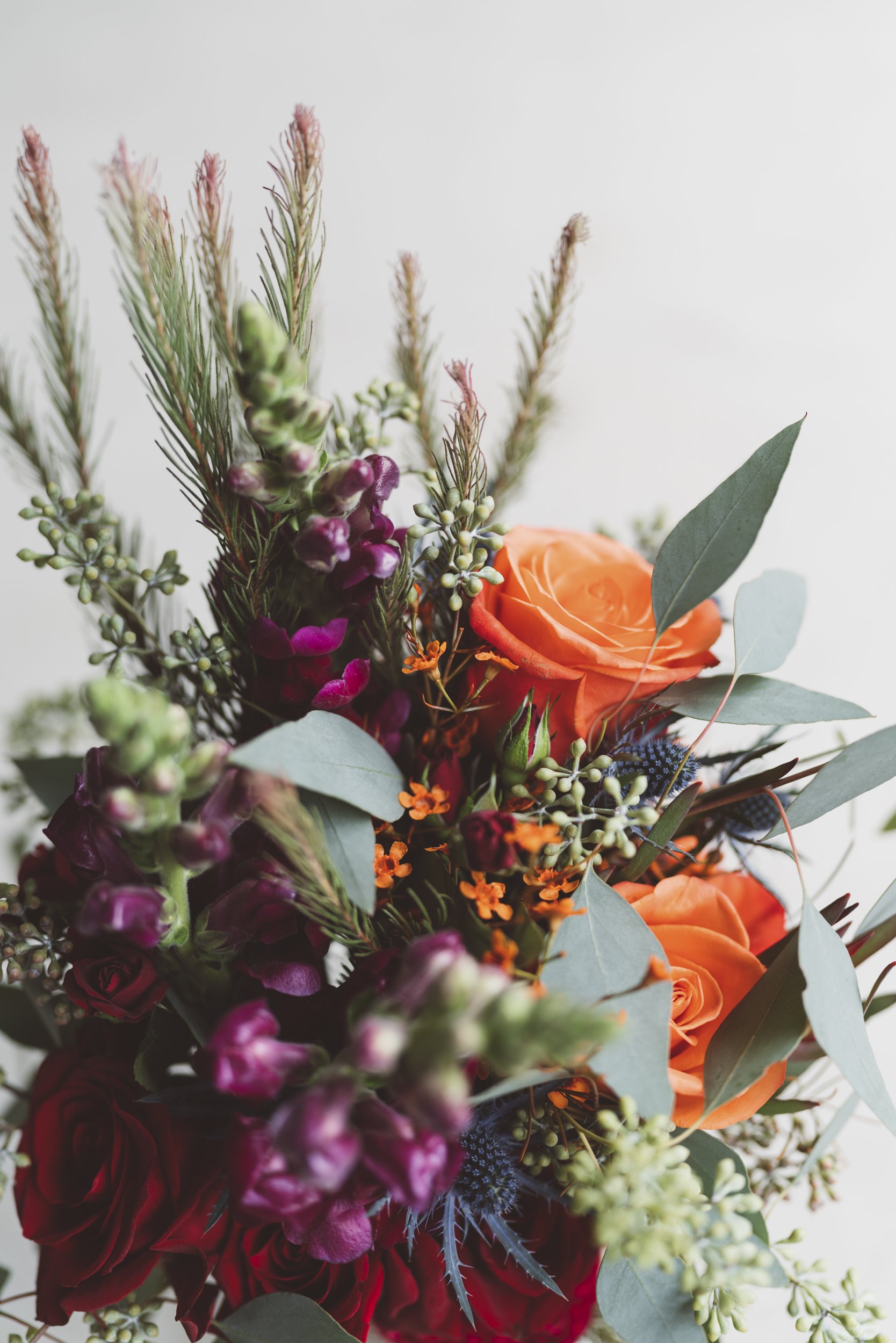 Close-up of a colorful flower bouquet featuring orange roses, purple flowers, green foliage, and small orange accents.