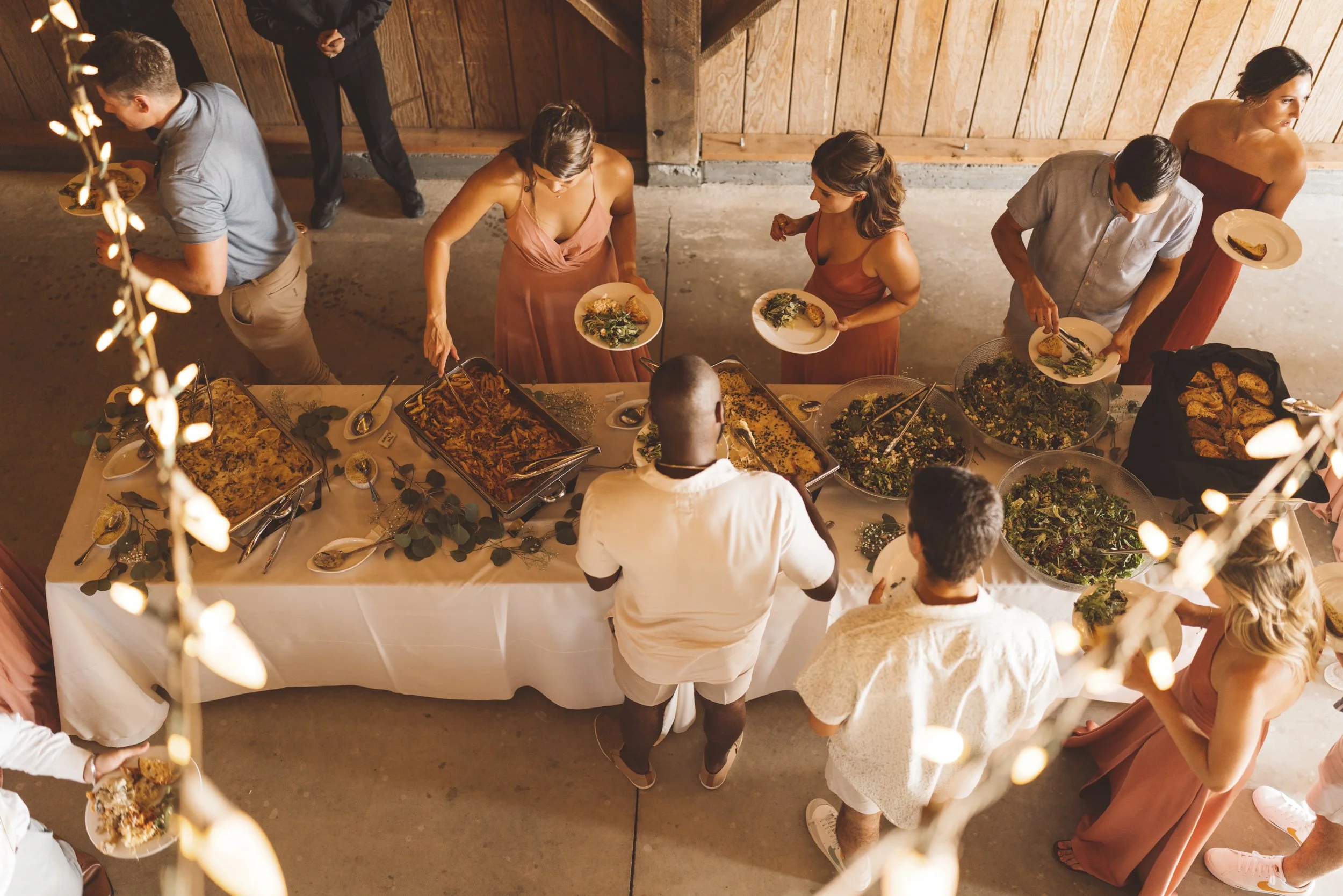 Guests serving themselves food at a buffet table during a gathering in a rustic setting.