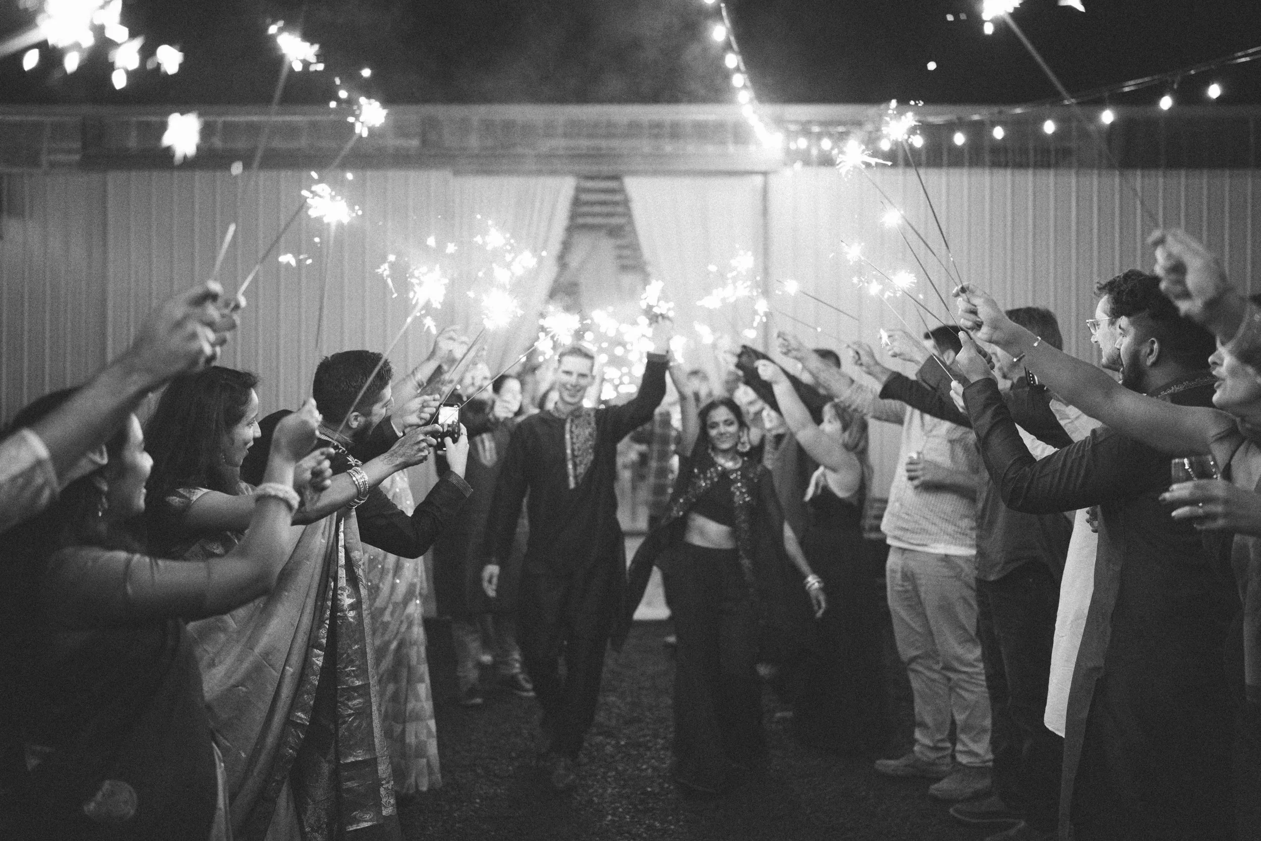 People celebrating a wedding with sparklers, forming a tunnel for the bride and groom to walk through at night.