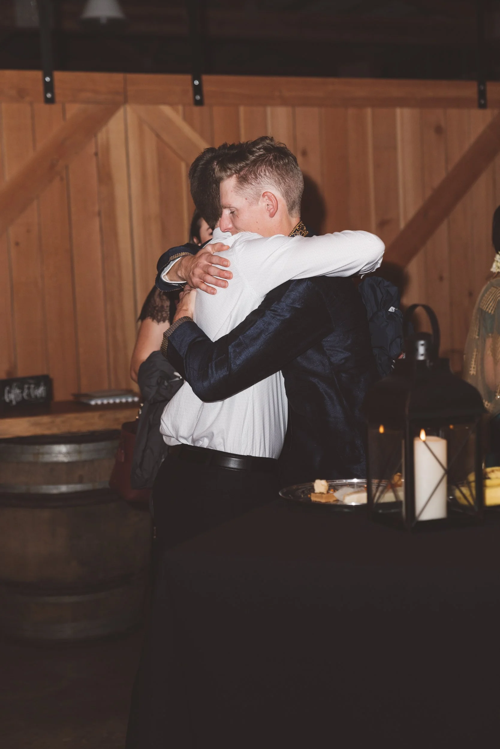 Two people hugging each other in a warmly lit indoor setting with wooden walls, likely at a celebration or event.