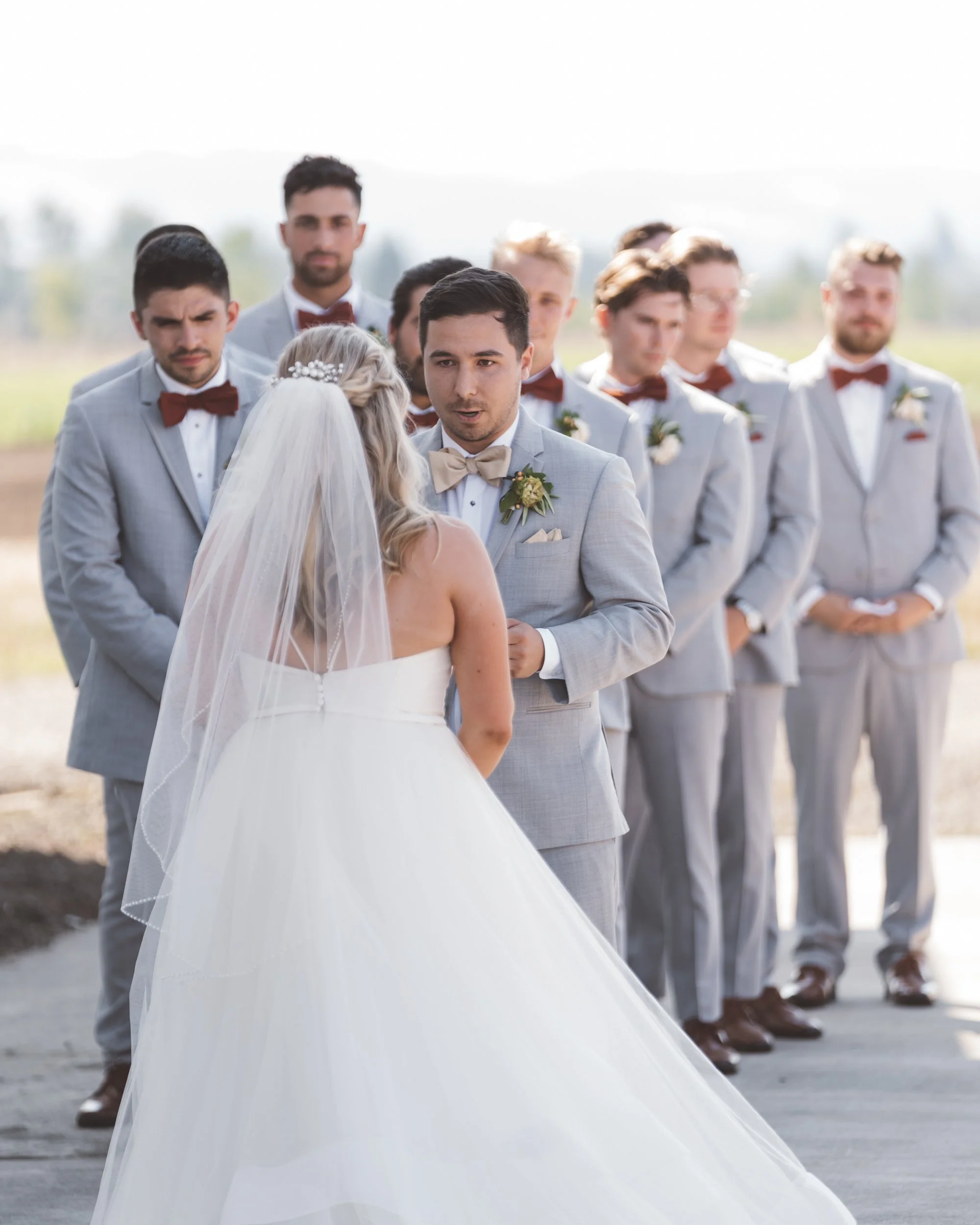 A bride and groom during their outdoor wedding ceremony, with groomsmen standing behind them.