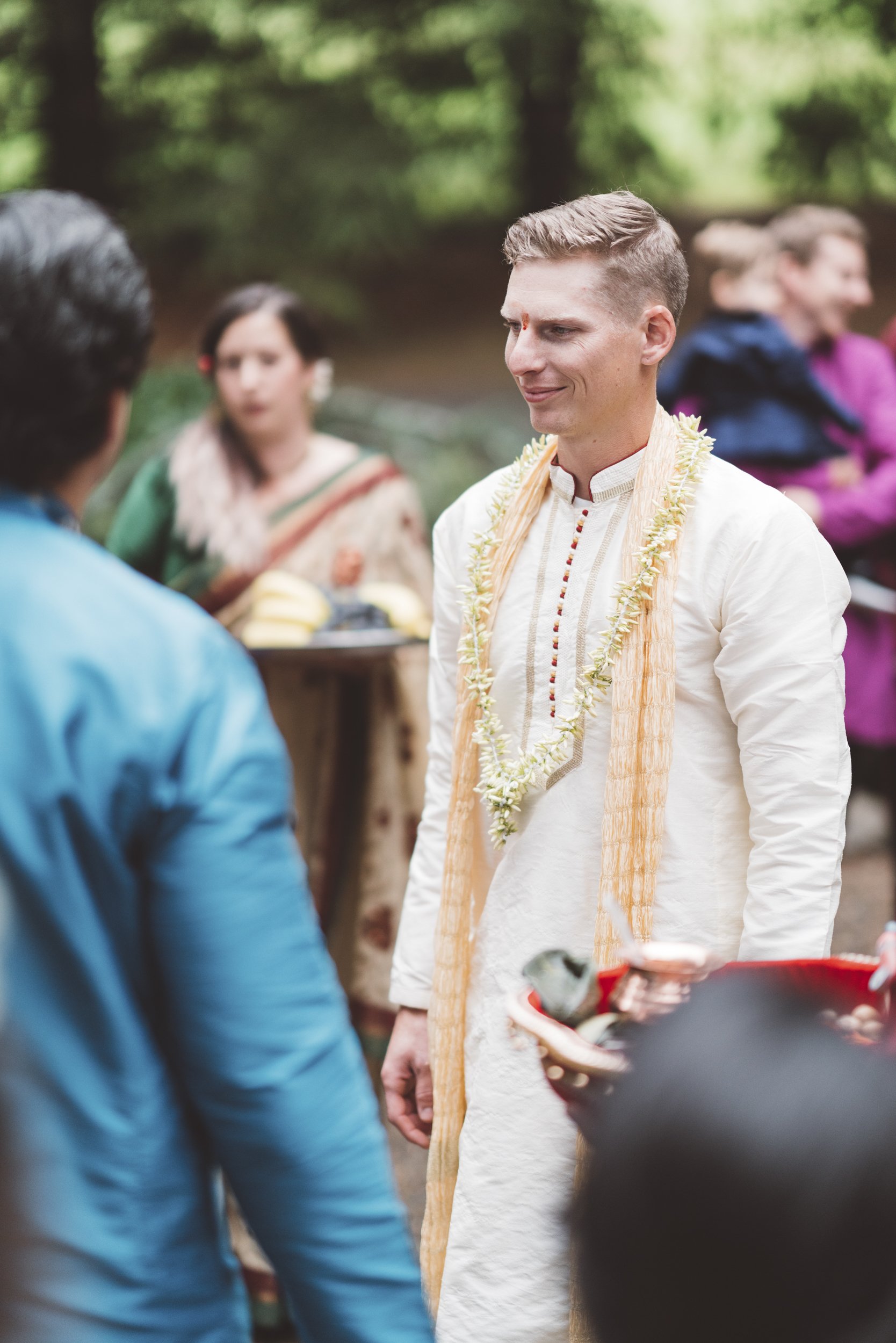 Man in traditional Indian attire wearing a flower garland during an outdoor ceremony.