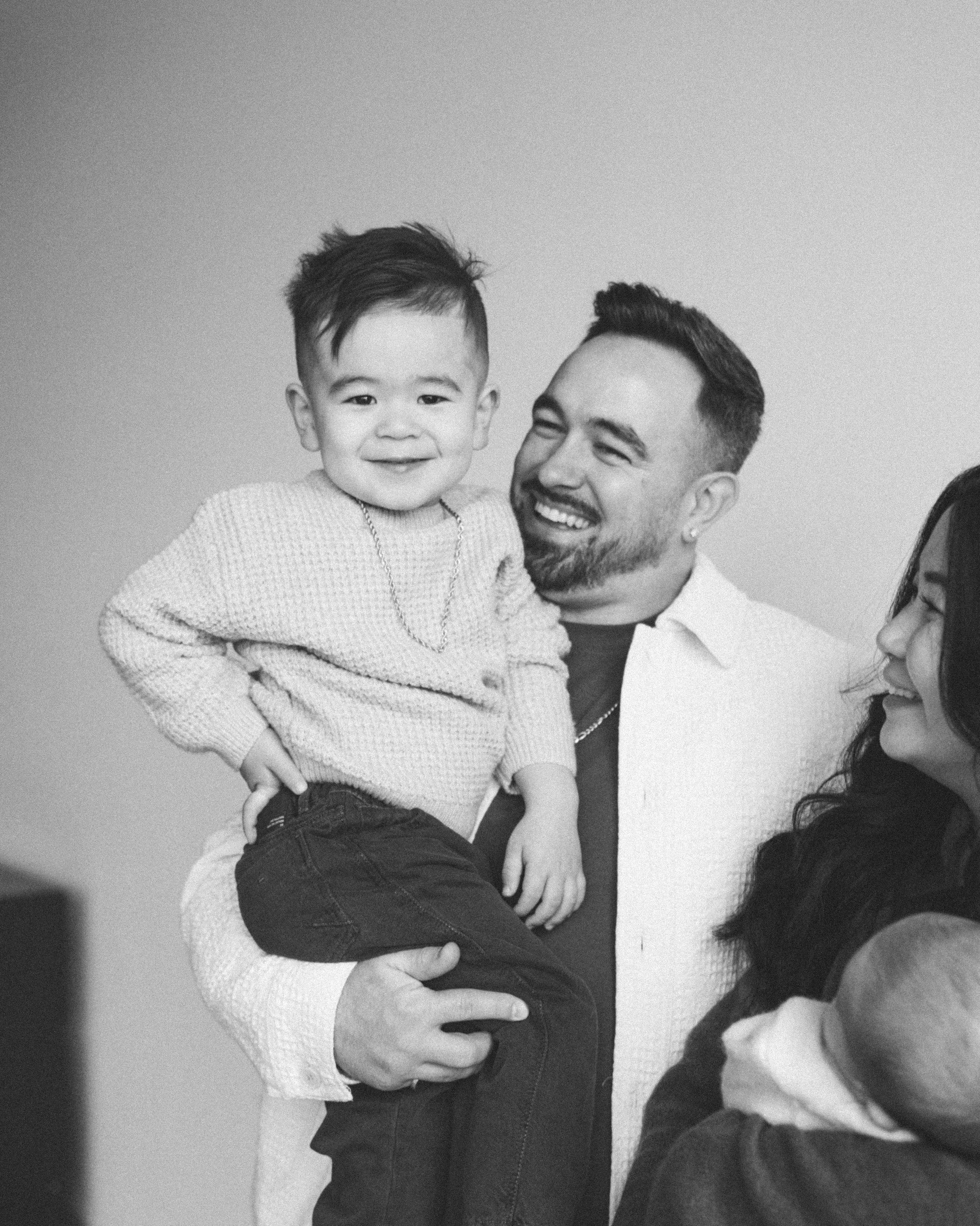 A man holding a smiling young boy, with a woman partially visible, all sharing a joyful moment.