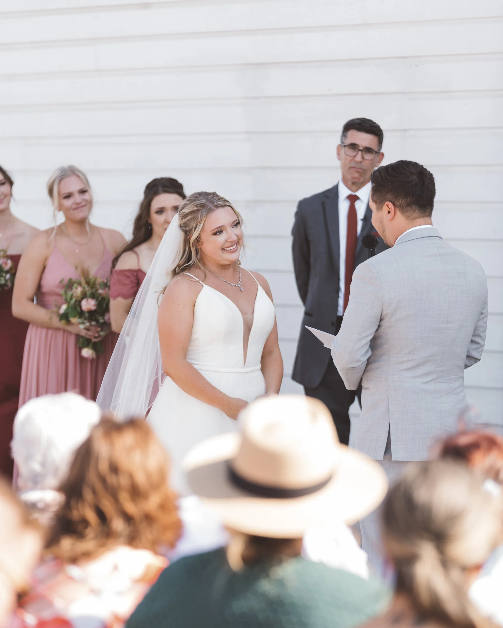 Bride and groom exchanging vows at an outdoor wedding with bridesmaids and guests watching.