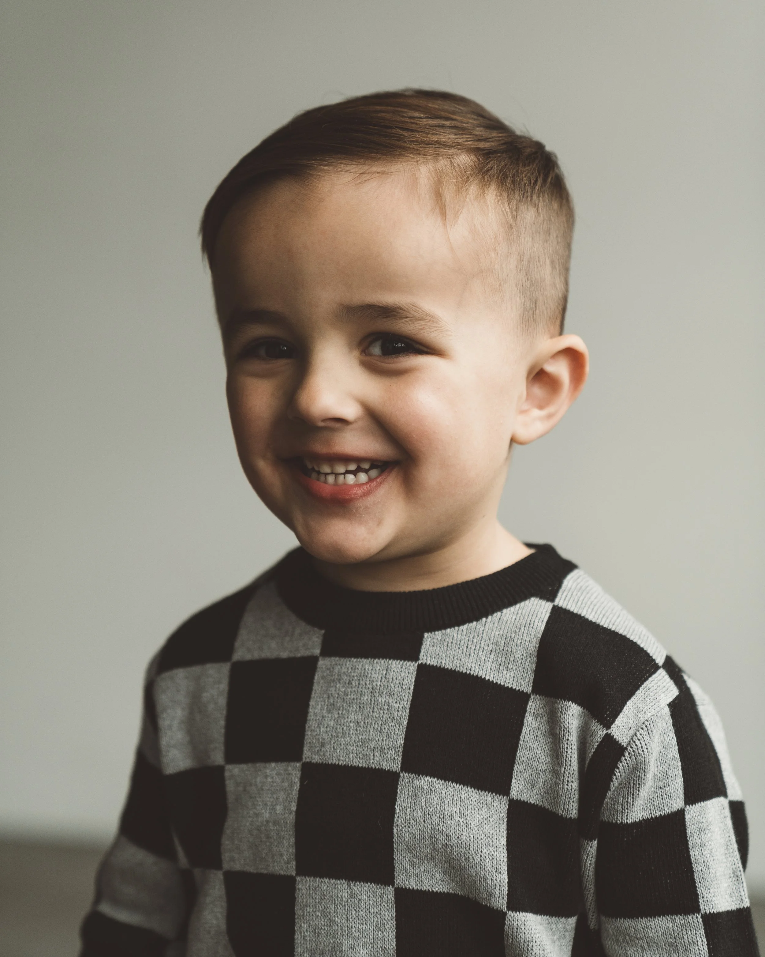 A young boy with brown hair smiling and wearing a black and gray checkered shirt.