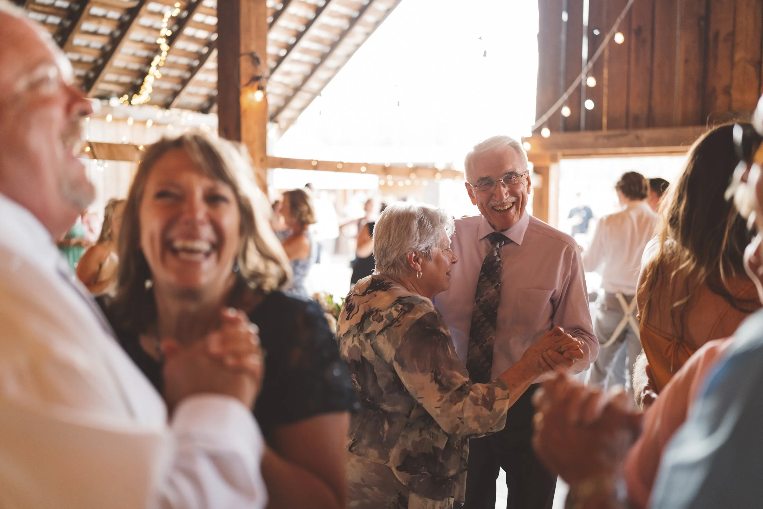 People dancing and celebrating in a rustic barn with string lights, smiling and enjoying a joyful moment.