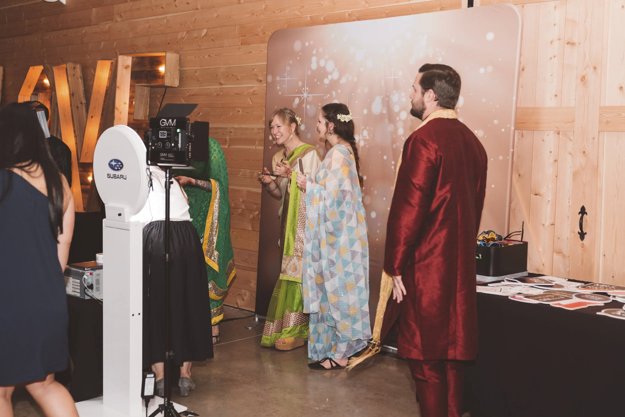 People dressed in traditional Indian attire at a party with a photo booth and festive decorations.