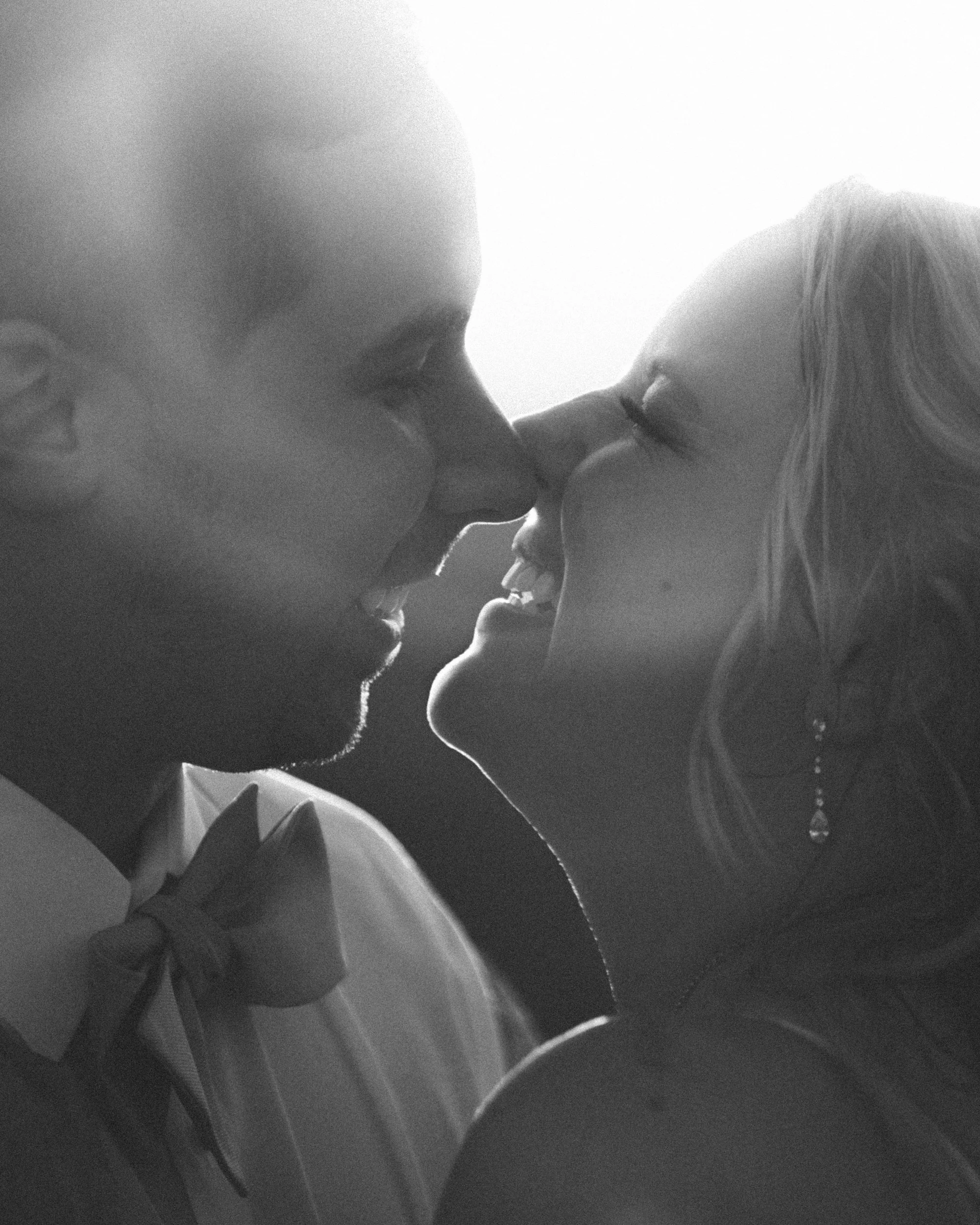 A black and white photo of a man and woman close to each other, nose to nose, about to kiss.