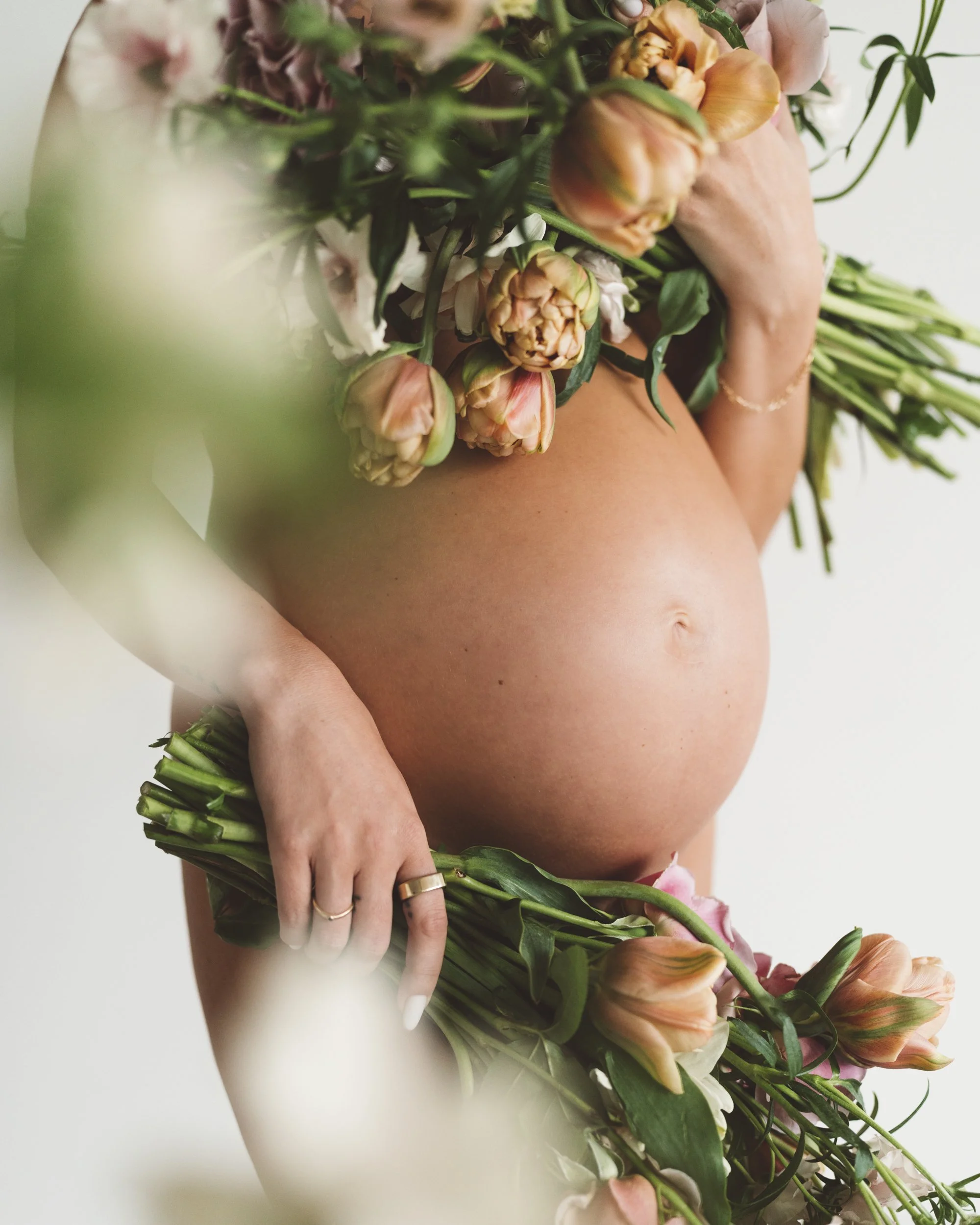 Close-up of a pregnant woman holding a bouquet of flowers covering her chest and lower body.