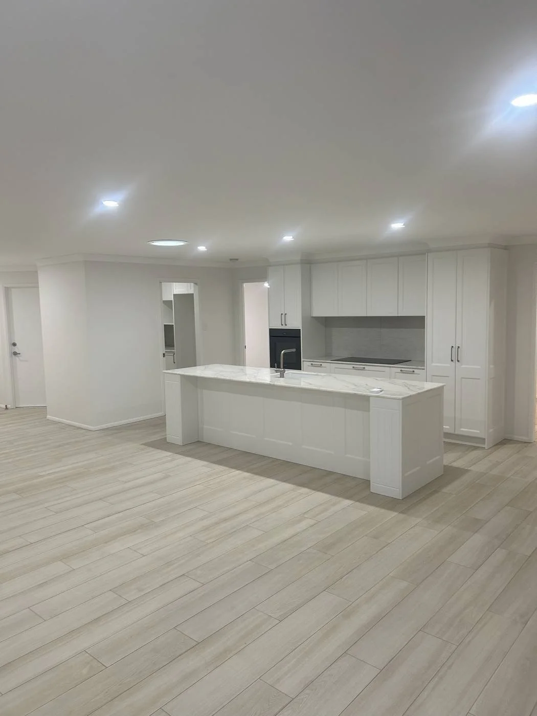 Open-plan kitchen renovation in Toowoomba with white shaker cabinetry, stone island benchtop and timber-look tiled floor