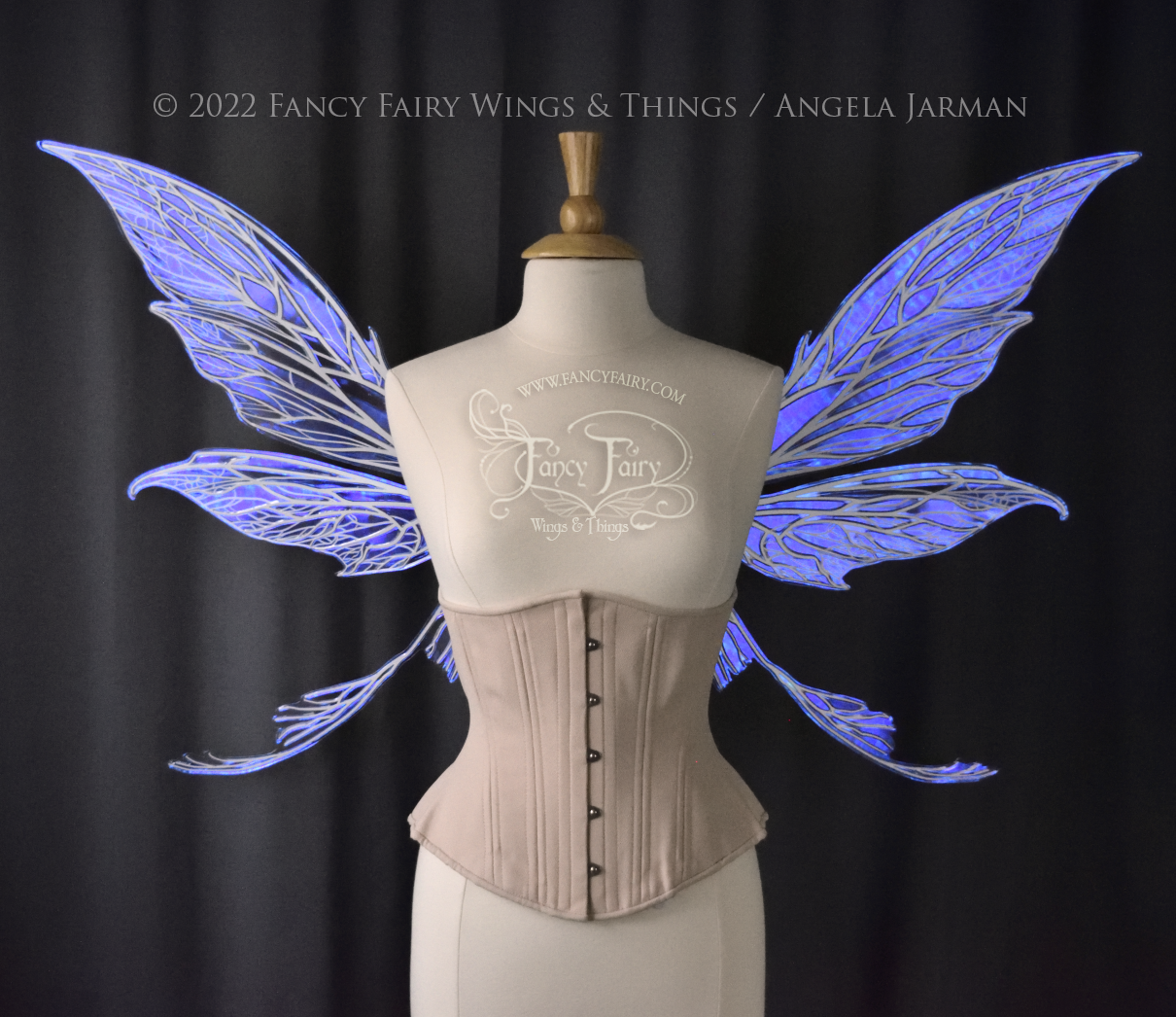  Front view of an ivory dress form wearing an alabaster underbust corset and large violet iridescent fairy wings with white veins. Upper panels are elongated with pointed tips, curved ‘tail’, lots of thin vein detail 