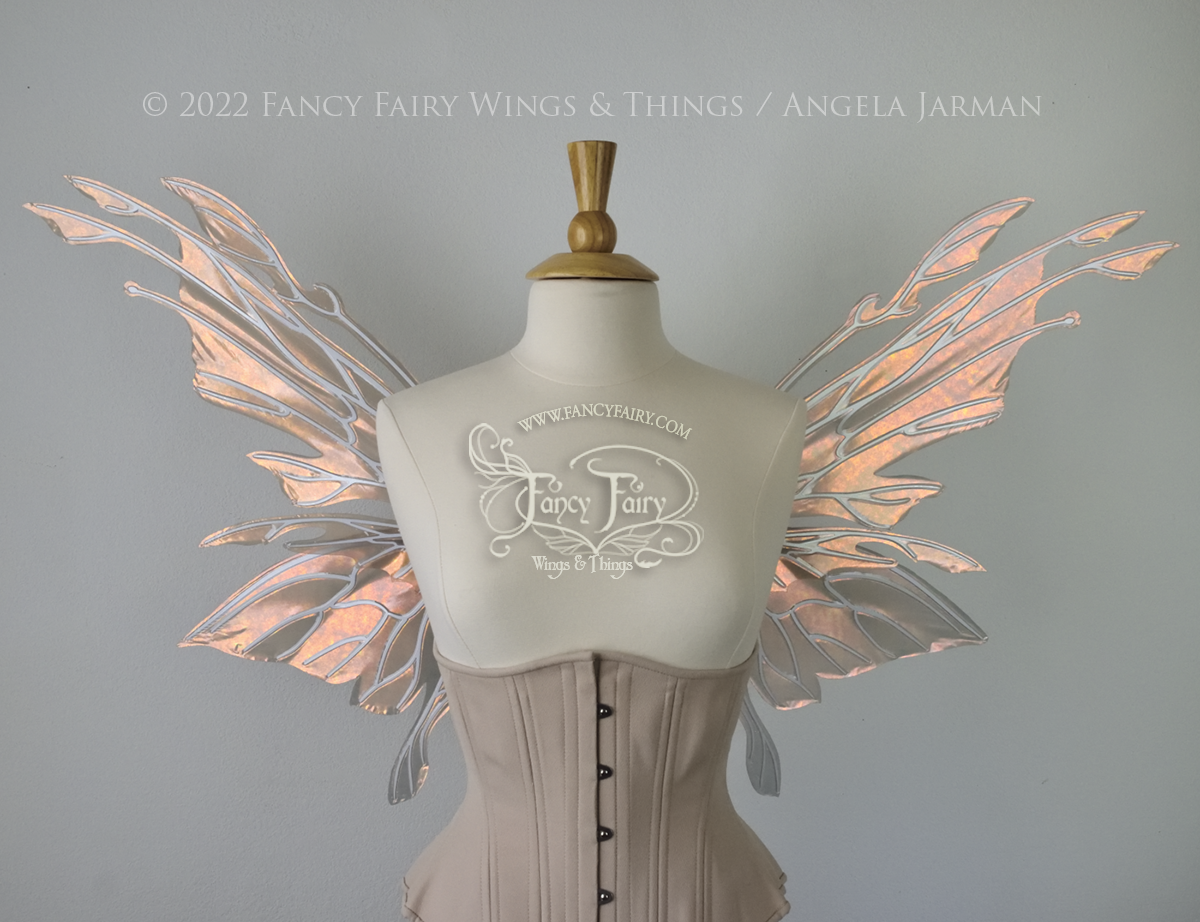  Front view of an ivory dress form wearing an alabaster underbust corset &amp; large rose gold iridescent fairy wings with elongated upper panels with petal like appendages at the tips &amp; antennae, the veins are white 