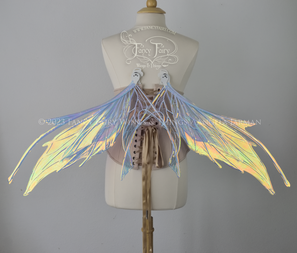  Back view of an ivory dress form wearing an alabaster underbust corset and large multicolor iridescent fairy wings in resting position, featuring antennae along the top. Upper panels come to a point as do the middle panels, bottom panels have tails.
