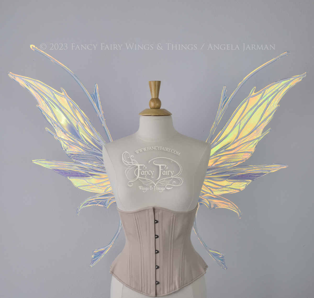  Front view of an ivory dress form wearing an alabaster underbust corset and large multicolor iridescent fairy wings featuring antennae along the top. Upper panels come to a point as do the middle panels, bottom panels have tails. Spikey, detailed wh