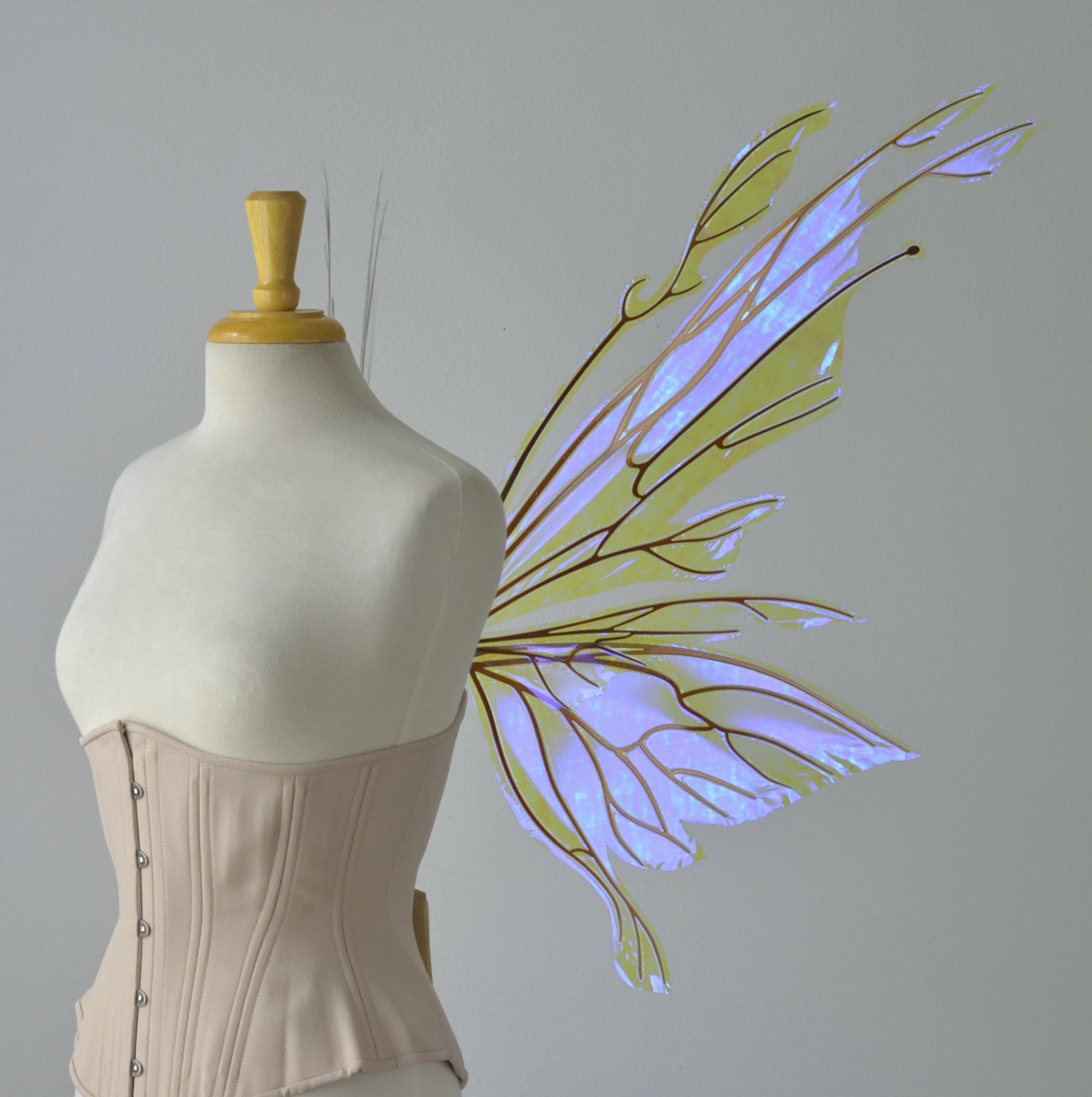  Right side view of an ivory dress form wearing an alabaster underbust corset &amp; large violet iridescent fairy wings with elongated upper panels with petal like appendages at the tips &amp; antennae, the veins are copper 