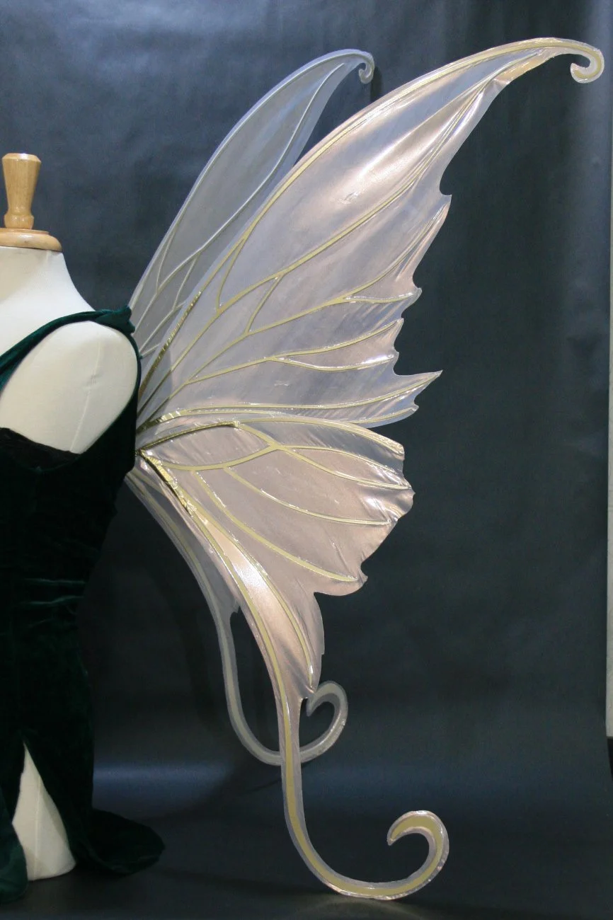Photo of a dress form wearing large shimmery pearl gold fairy wings with curled tips against a dark background
