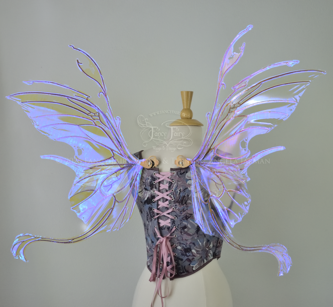 Large violet transparent iridescent fairy wings with a spikey profile and curvy tails on bottom, worn on a dress form, back view.