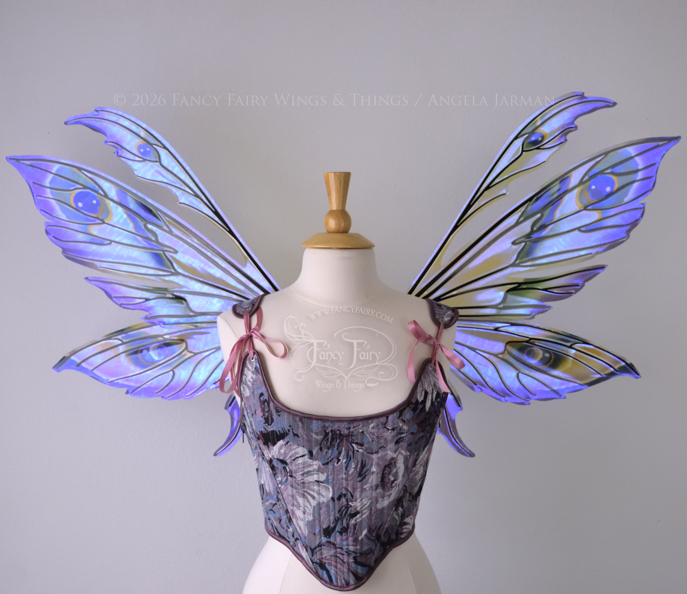 Large transparent fairy wings with antennae have peacock 'eye' accents painted on violet iridescent film with black veins, worn on dress form, front view
