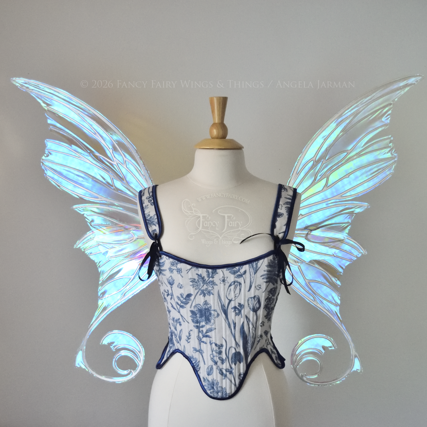 Front view of an ivory dress form wearing large transparent blue & green iridescent fairy wings with lots of intricate silver veins, some have 'thorns'. Upper panels curve slightly downwards along top edge with pointy tips, bottom panels have tails