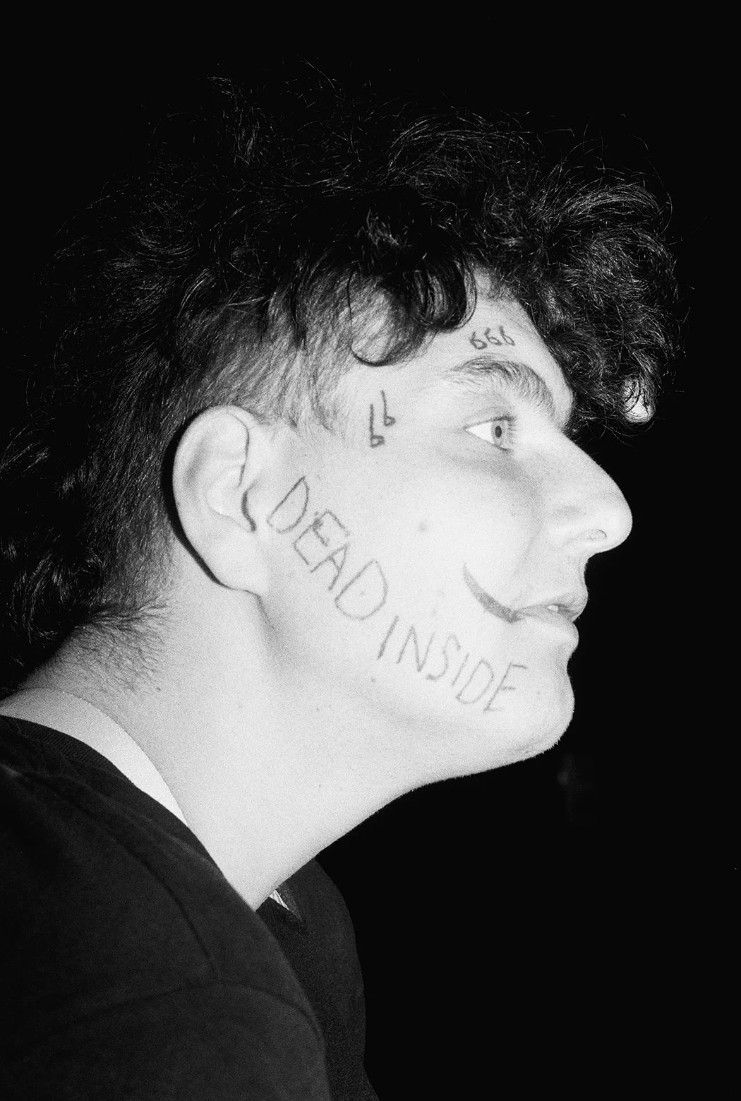 Close-up black and white photo of a person's face being pressed by a hand, with water streaming down the face and smiling teeth visible.