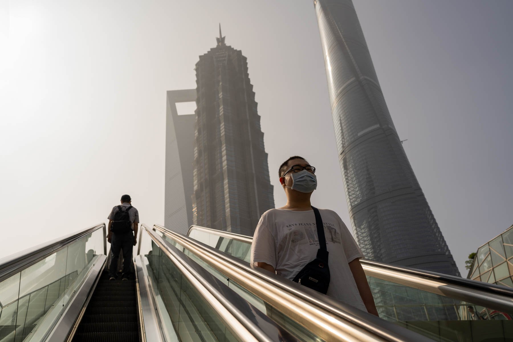  Pedestrians ride an escalator as the Shanghai World Financial Center Tower, left, Jin Mao Tower, center, and the Shanghai Tower, right, are seen in Pudong's Lujiazui Financial District in Shanghai, China on Wednesday, June 21, 2023. 