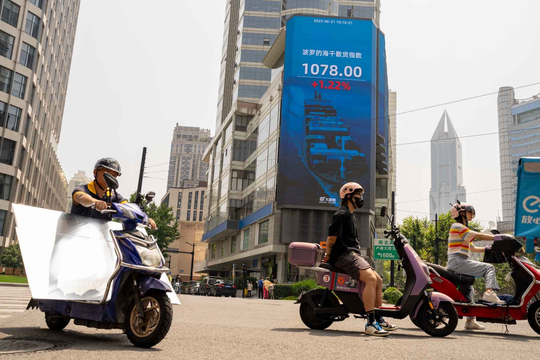  Motorcyclists ride past a public screen displays stock figures in Shanghai, China on Wednesday, June 21, 2023. 