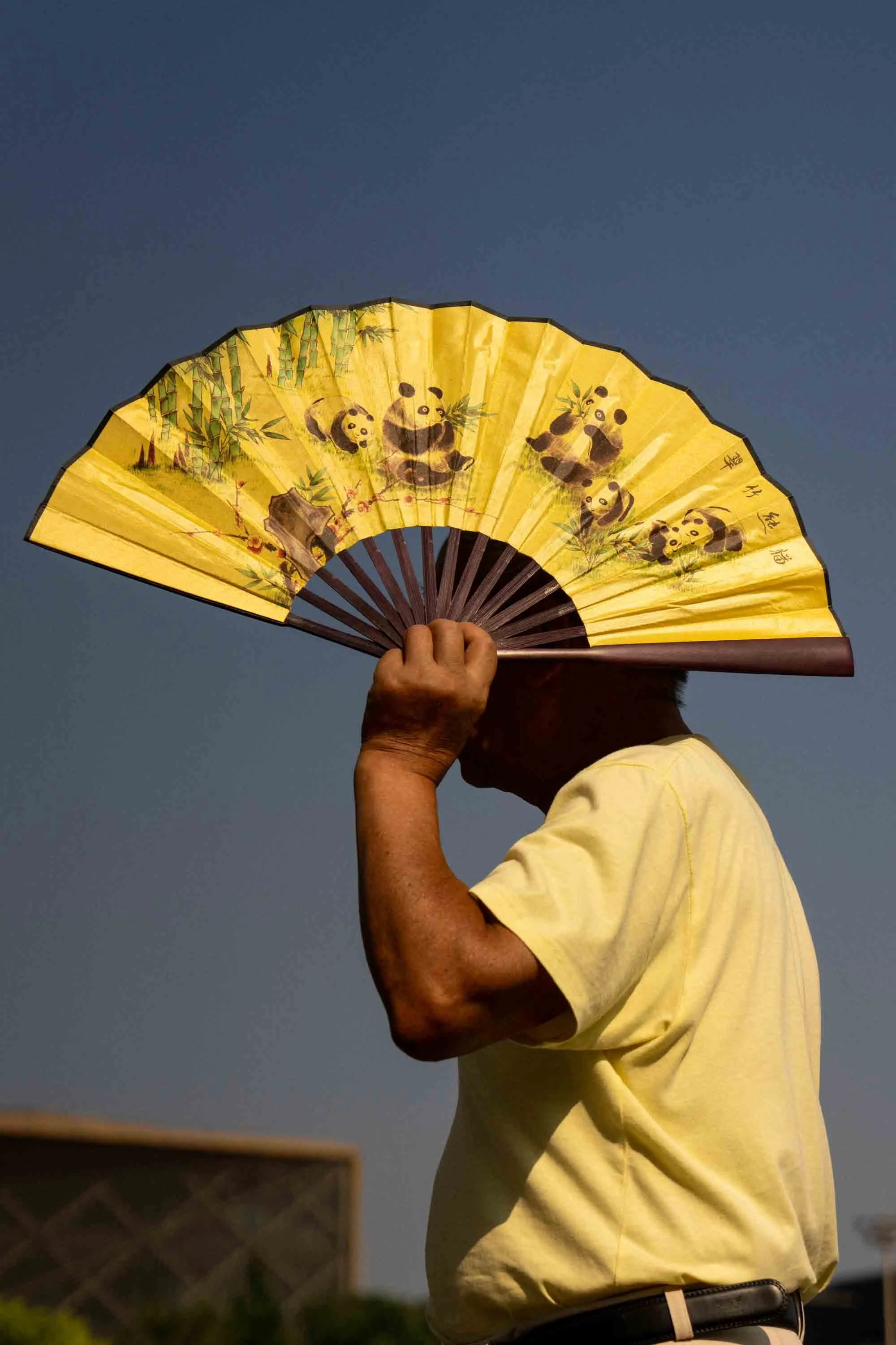 Person holding a decorative yellow paper fan with panda illustrations against a clear blue sky.