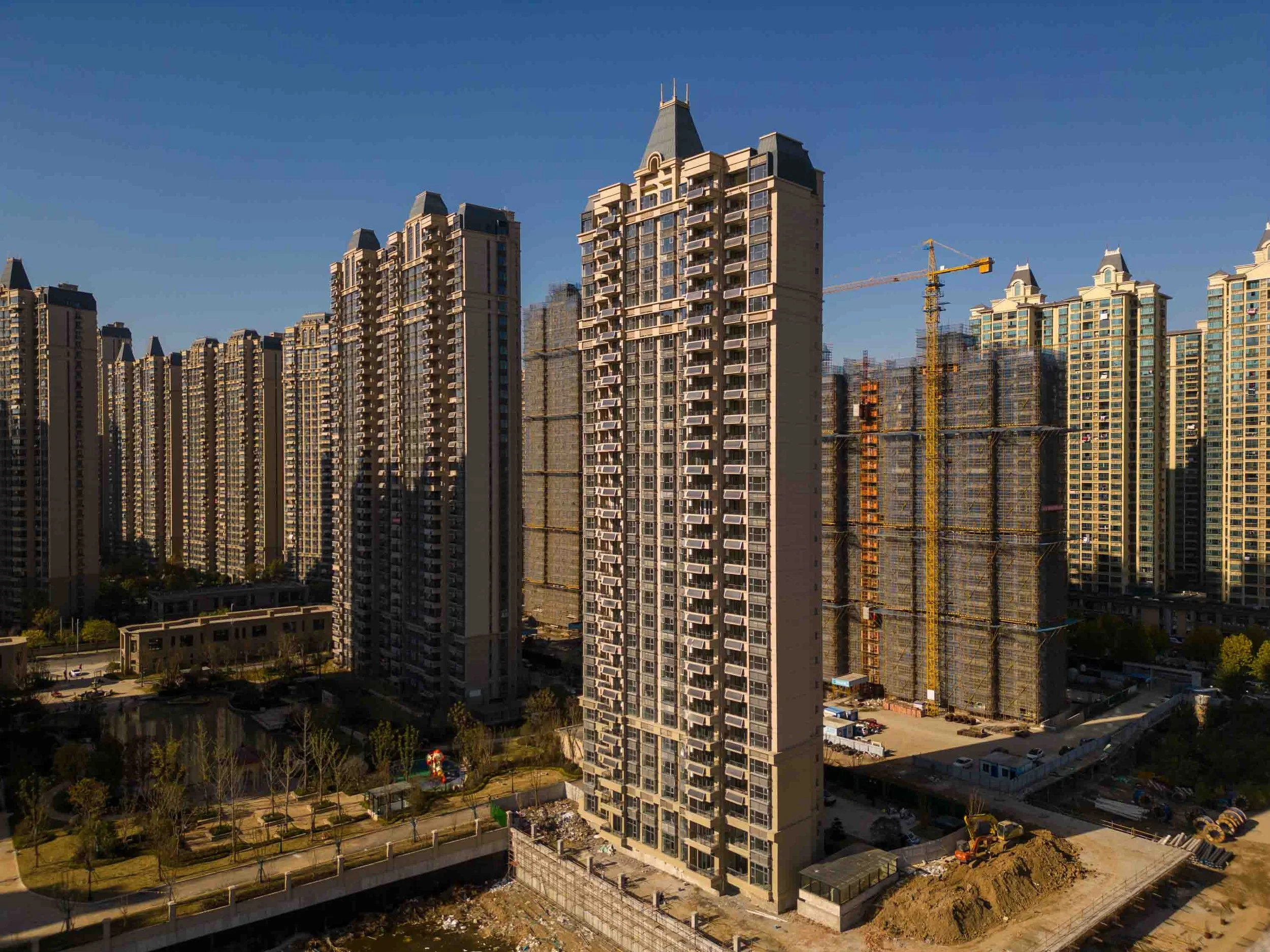 High-rise residential buildings under construction in an urban area with a construction crane and a clear blue sky.