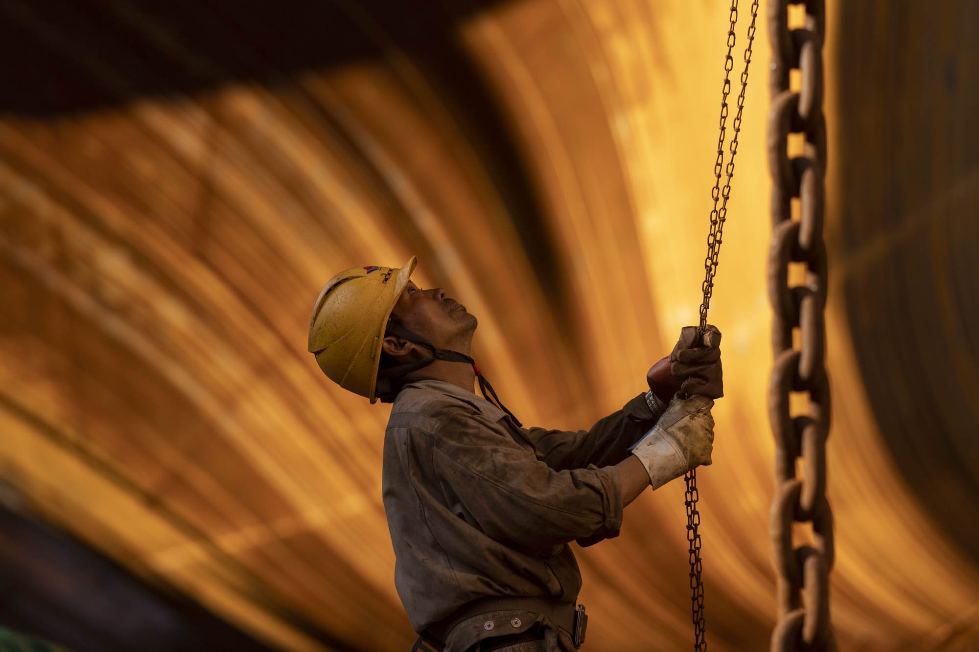A construction worker wearing a helmet holding onto a chain inside a tunnel.