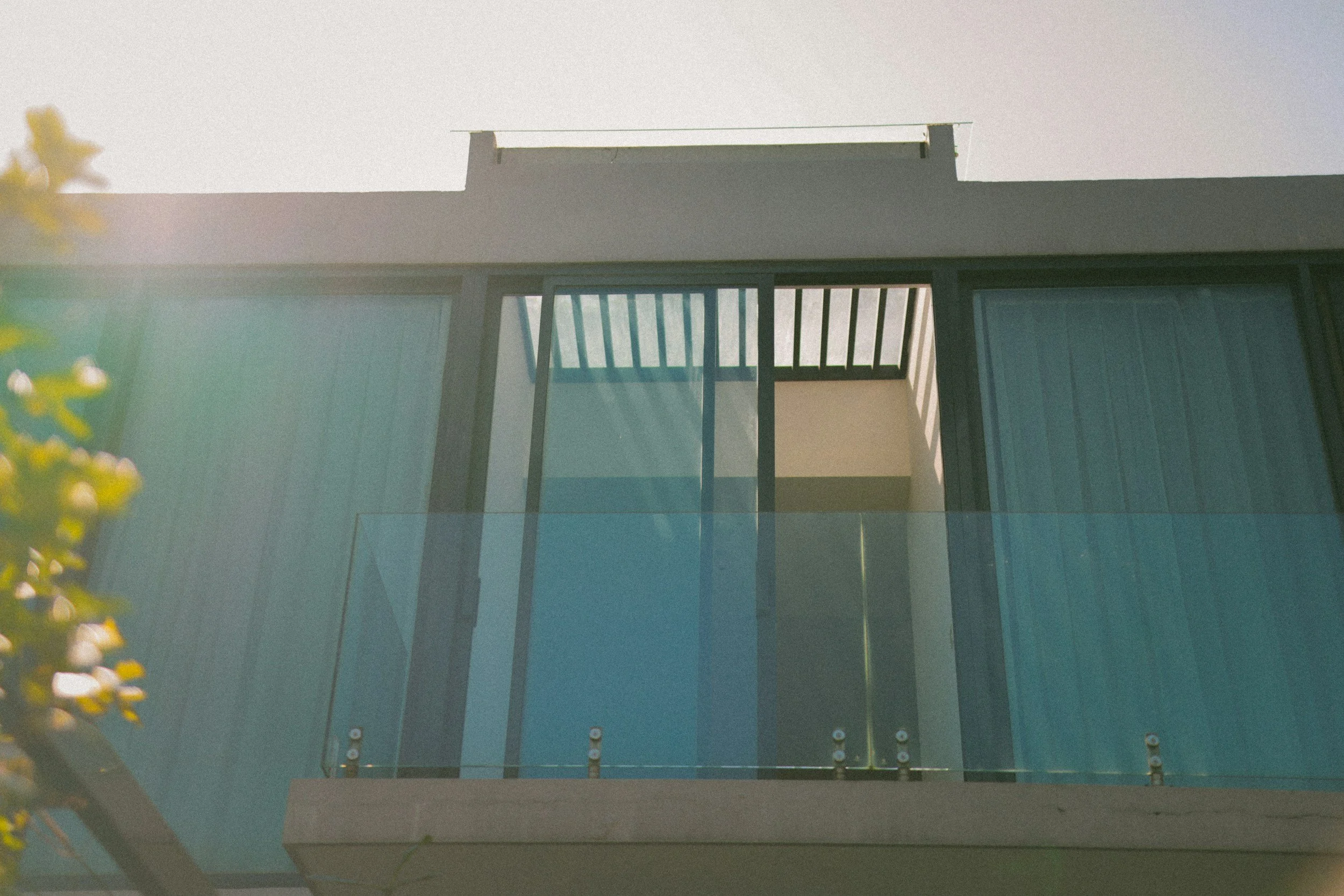 Modern building with glass balcony and large sliding glass doors, sunlight shining from the left.