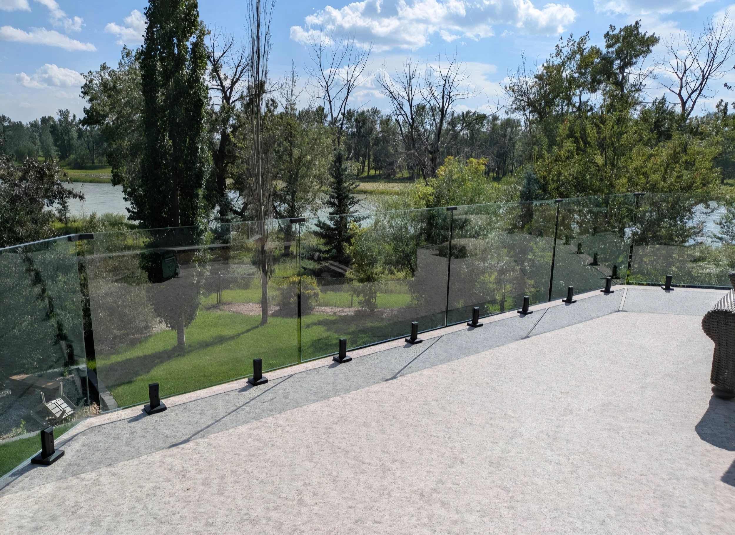 Balcony with glass railing overlooking a lush green landscape and river, under a partly cloudy sky.