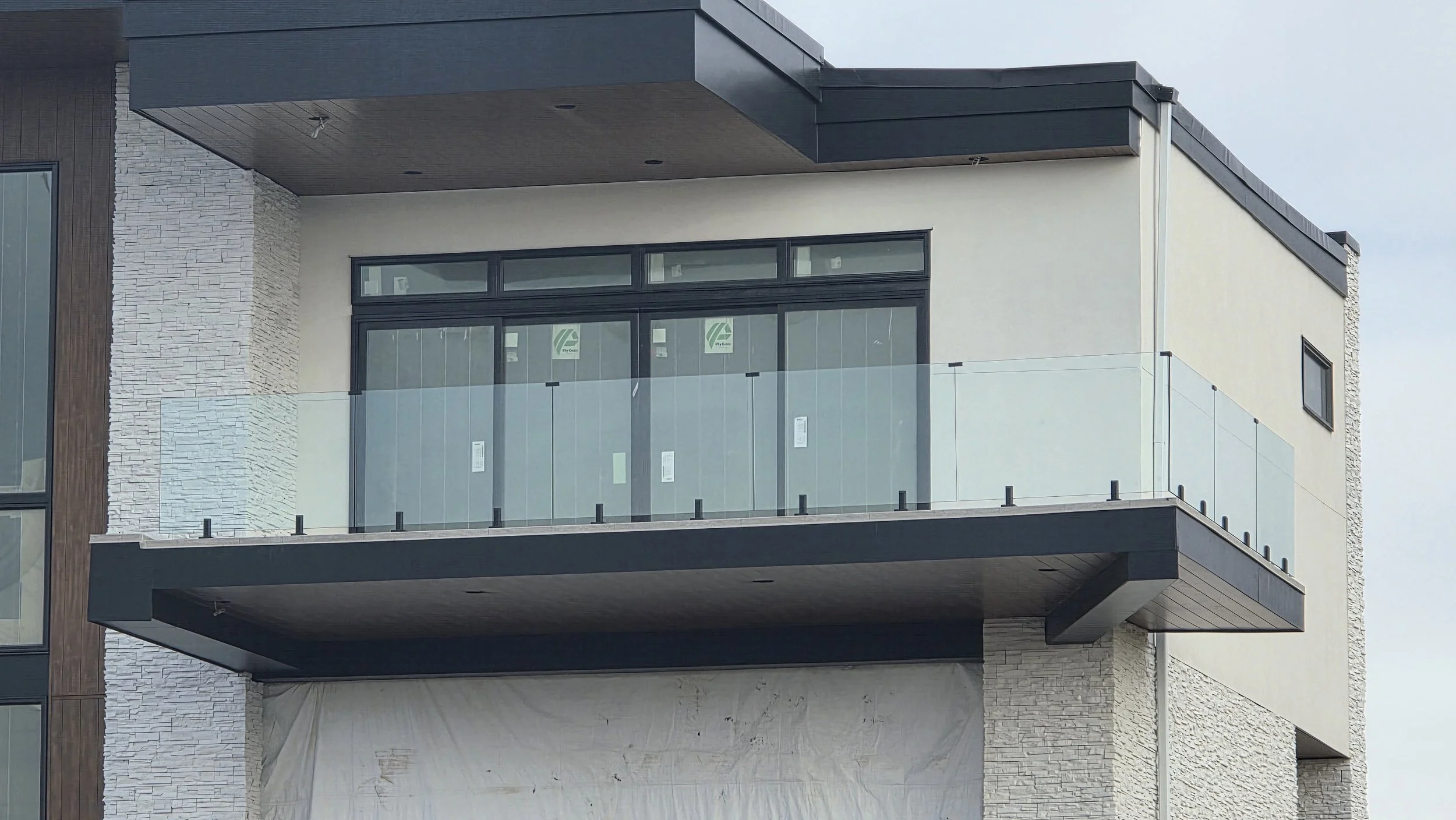 Modern multi-story building with glass balcony, dark trim, light stucco and stone exterior.