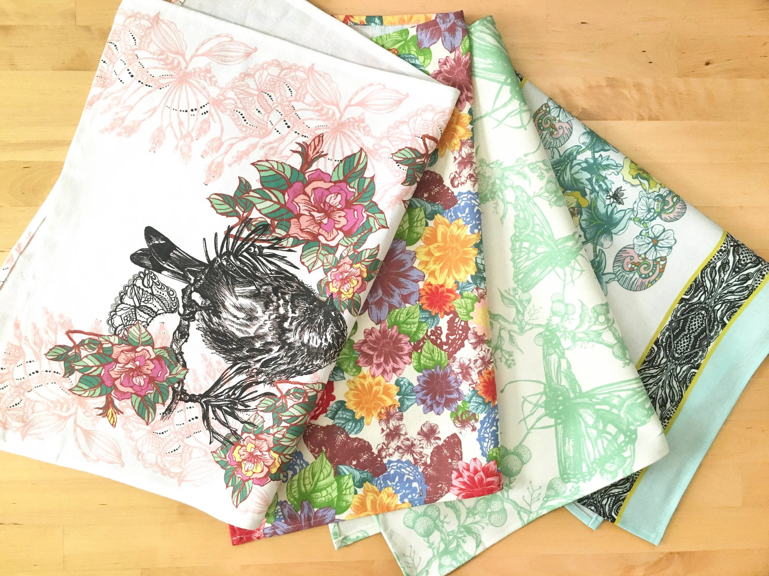 Four Janice Nelson kitchen tea towels folded in half laying side by side