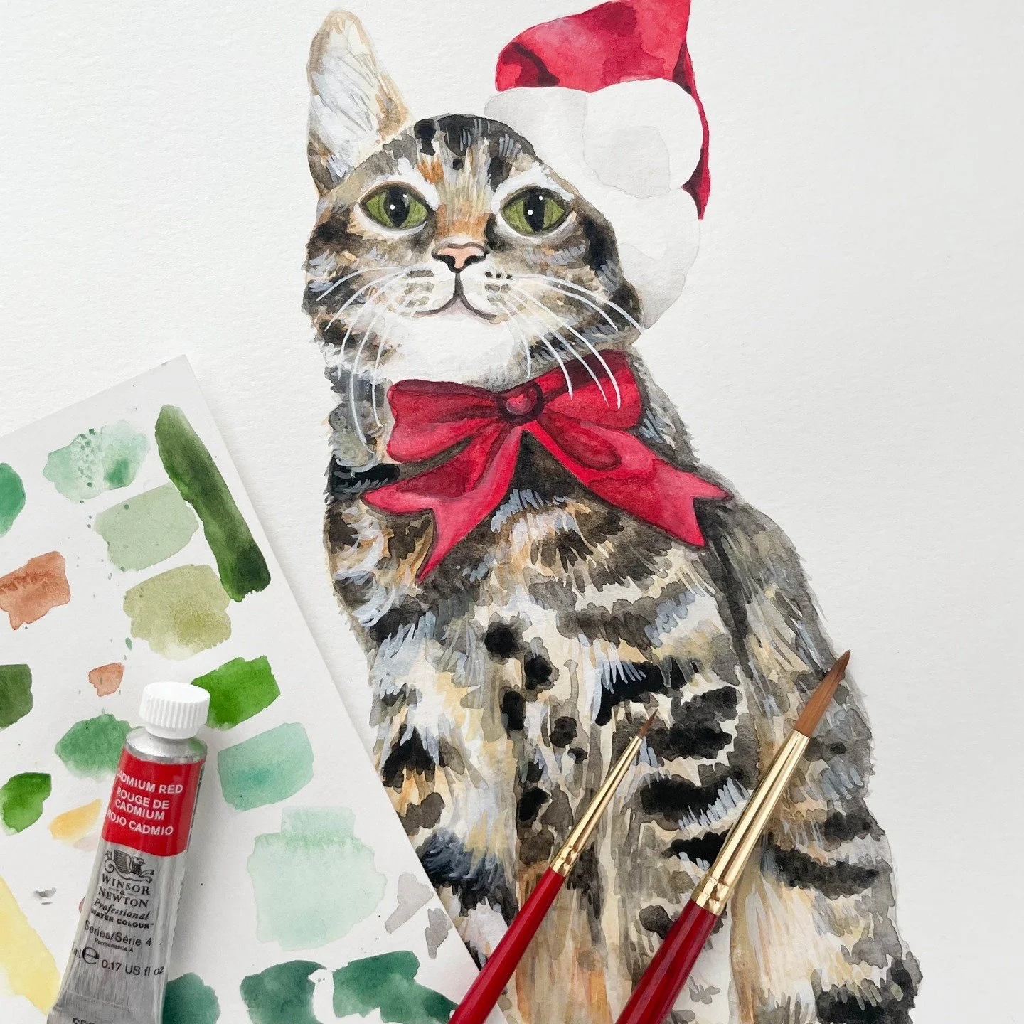 A very festive feline with a Santa hat, a big red bow, and bright green eyes! 🎄🐈