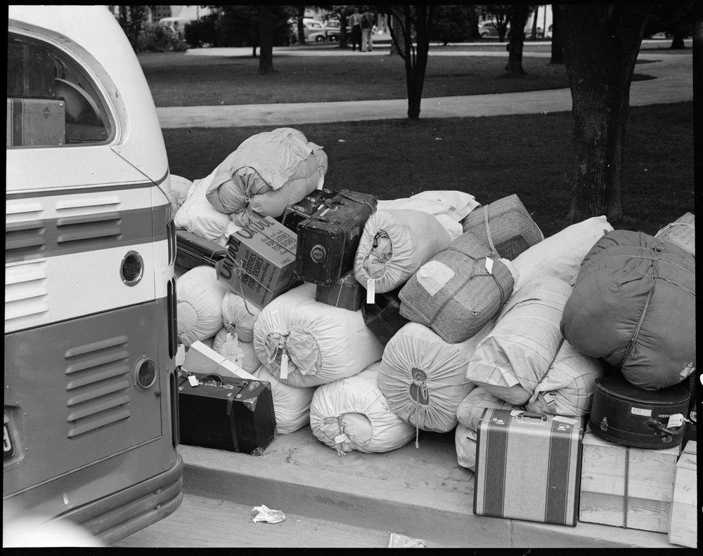  Hayward, California. Baggage of evacuees of Japanese ancestry stacked at public park as evacuation bus prepares to leave for Tanforan assembly center. Evacuees will be transferred later to War Relocation Authority centers where they will spend the d