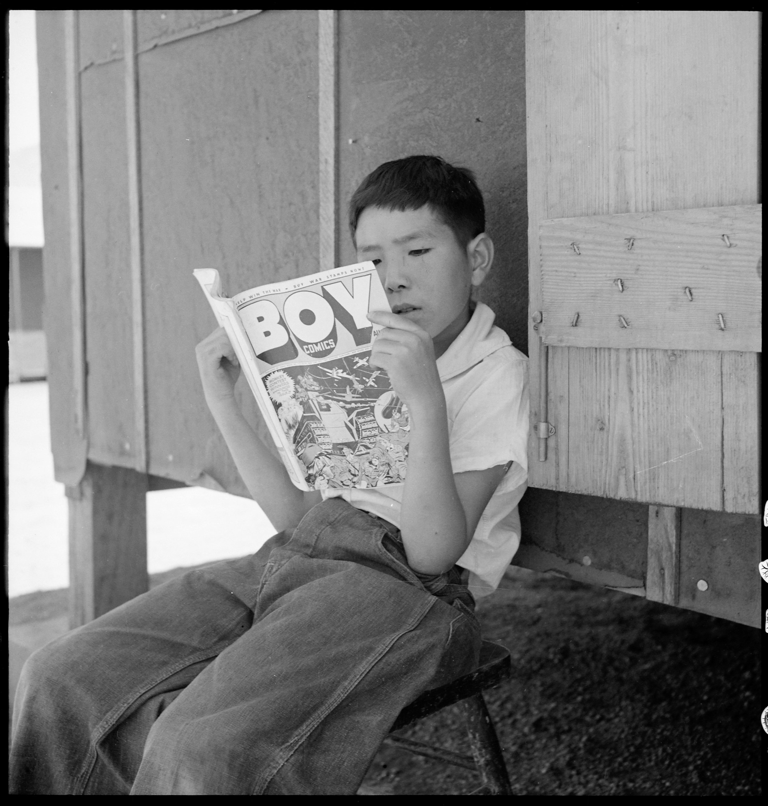  Manzanar Relocation Center, Manzanar, California. Evacuee boy at this War Relocation Authority center reading the Funnies. 