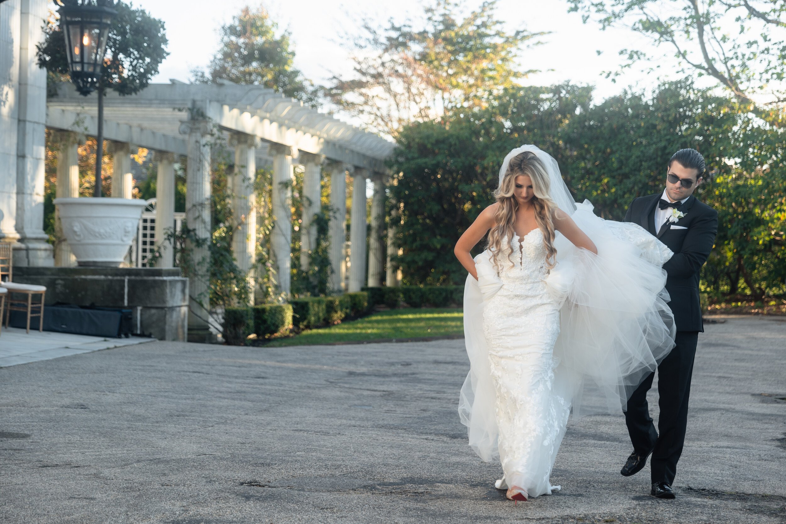 Gina and Anthony walking along Rosecliff's colonnaded loggia, her veil in motion, evening light through the columns.
