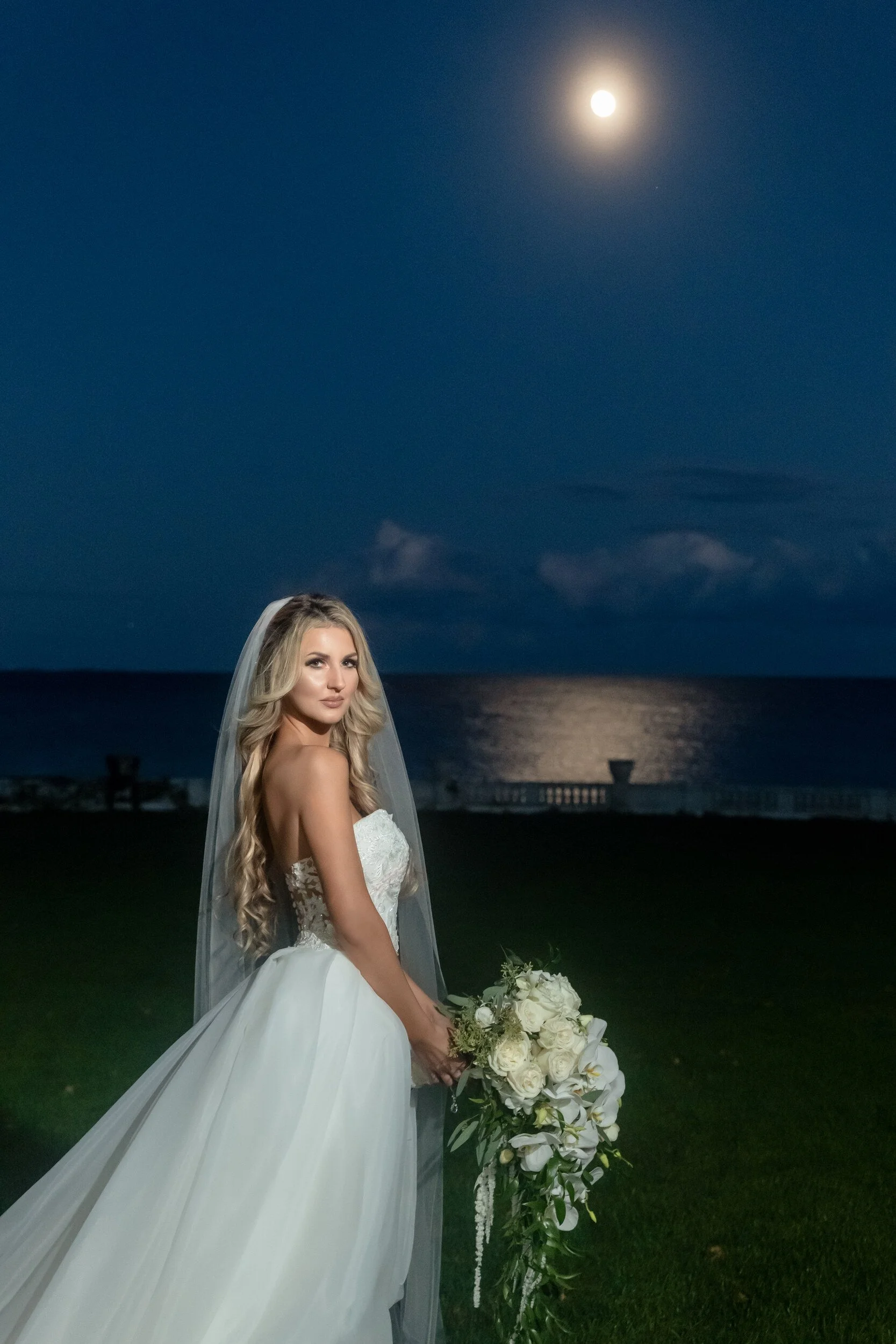 Gina looking back over her shoulder at dusk, the moon and the ocean behind her.