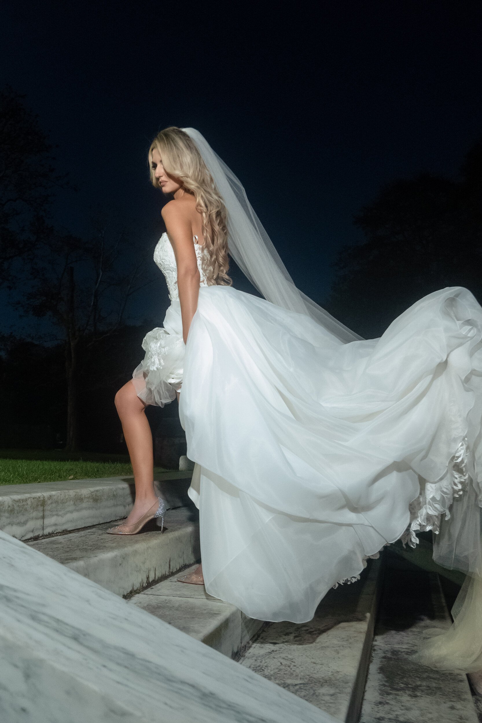 Bride standing on stone steps at Rosecliff at night, her veil and dress train cascading down the steps behind her.
