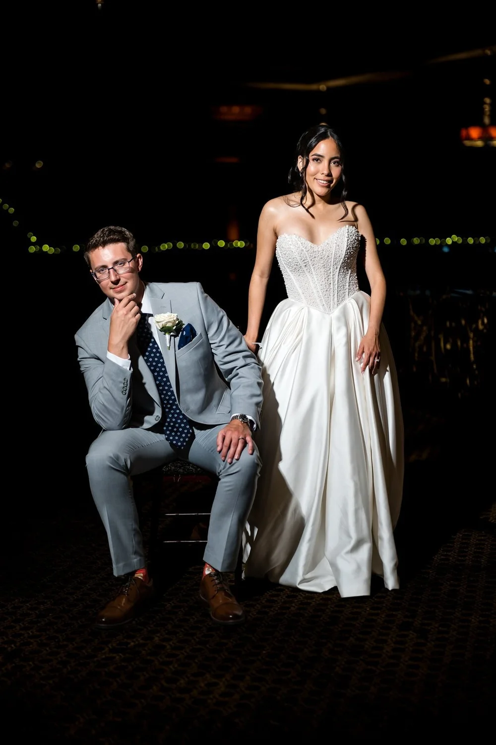 The Society Room of Hartford wedding photographer, Hartford, CT â€” dramatic evening portrait with the groom seated and the bride standing beneath string lights