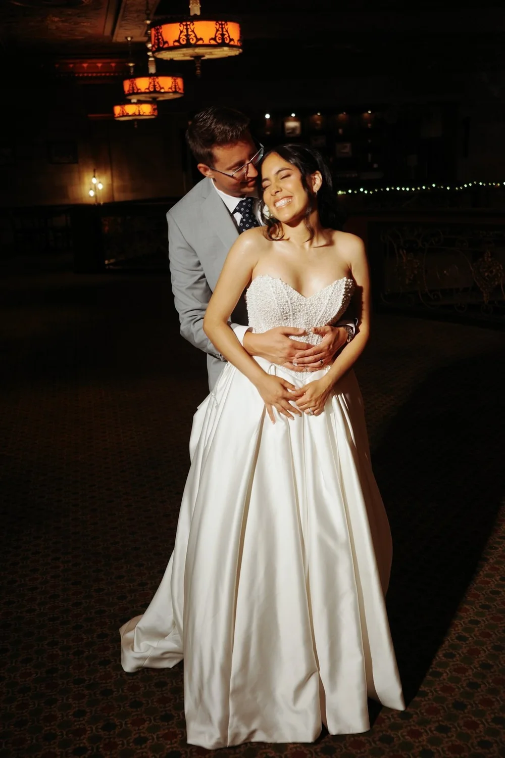 The Society Room of Hartford wedding photographer, Hartford, CT â€” groom holding the bride from behind under warm pendant lights