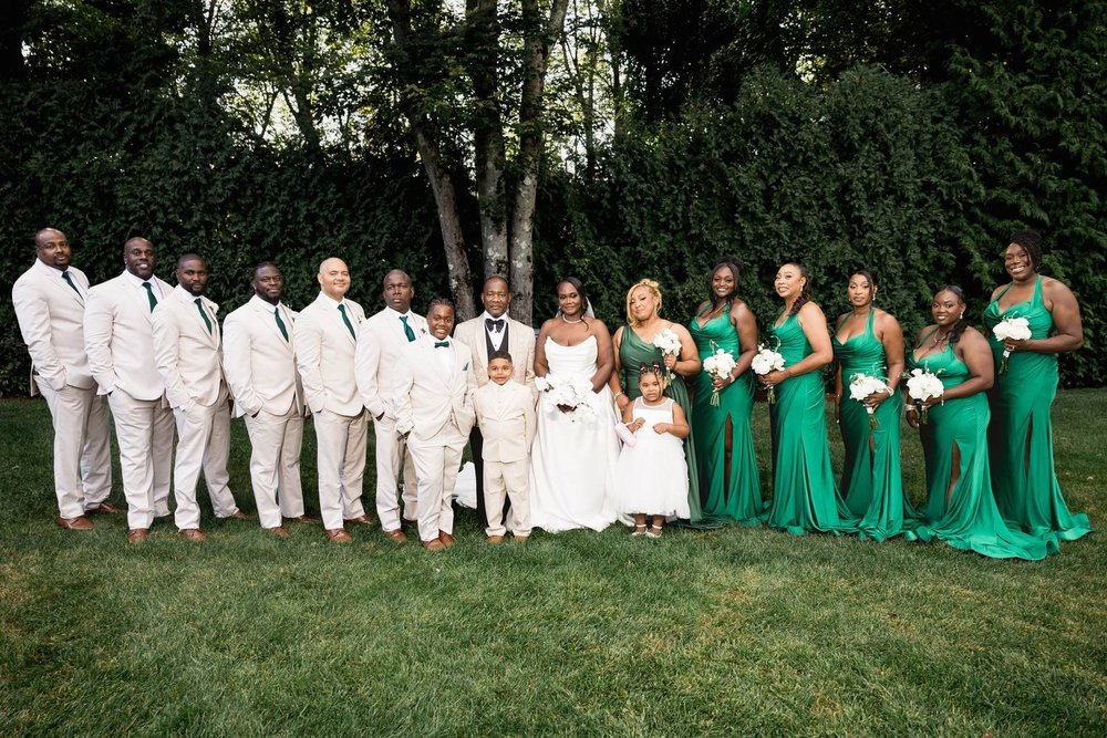 Avenir wedding photographer, Walpole, MA — full bridal party in emerald gowns and ivory tuxedos on the manicured ceremony lawn framed by woodland