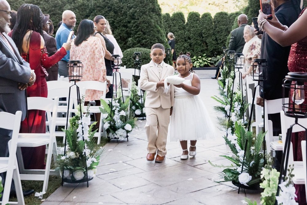 Avenir wedding videographer, Walpole, MA — outdoor garden ceremony aisle lined with white florals, white chairs, and clipped evergreen hedges