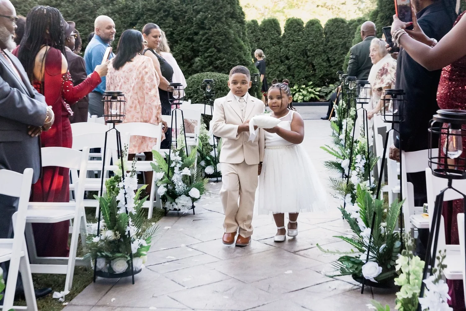 Avenir wedding videographer, Walpole, MA — outdoor garden ceremony aisle lined with white florals, white chairs, and clipped evergreen hedges