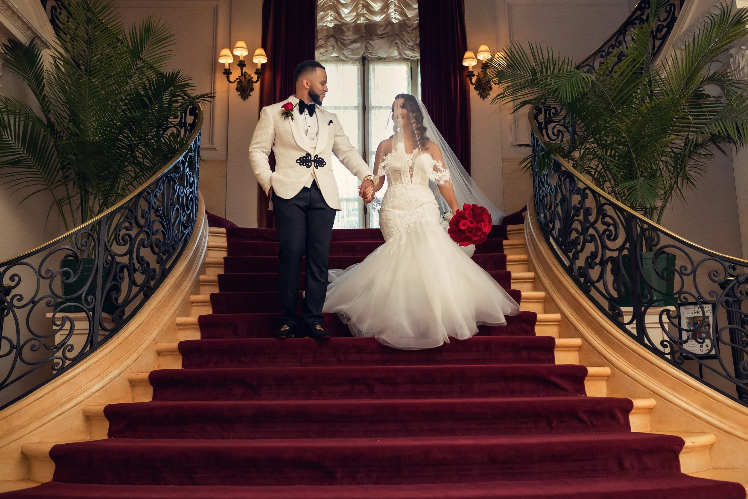 A couple coming down the red-carpeted heart-shaped staircase inside Rosecliff Mansion, Newport, Rhode Island