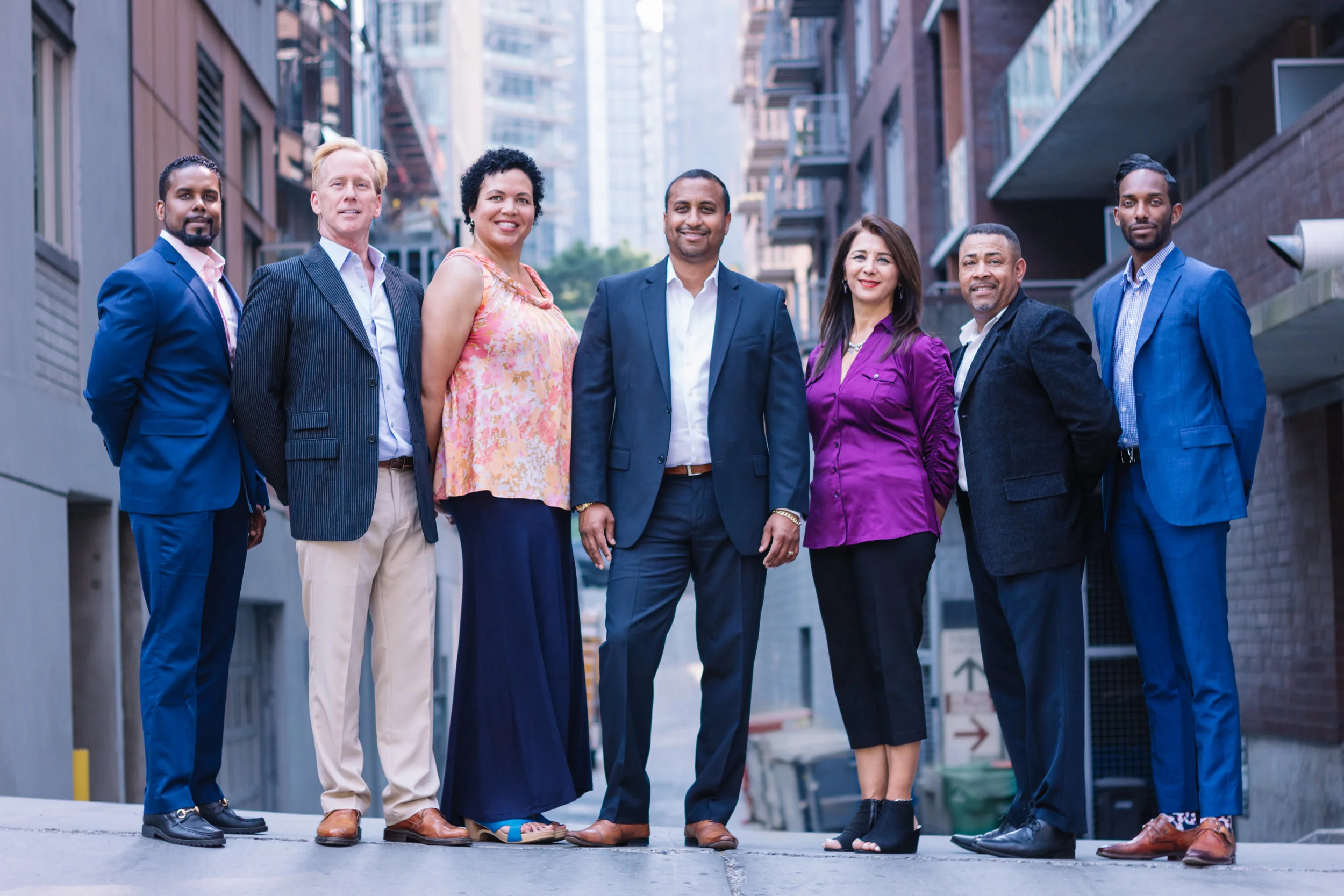 Group of eight diverse professionals standing together outdoors in an urban environment with buildings in the background.
