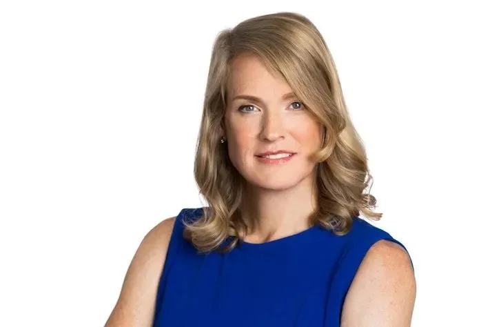 A woman with shoulder-length blonde hair wearing a sleeveless royal blue dress.
