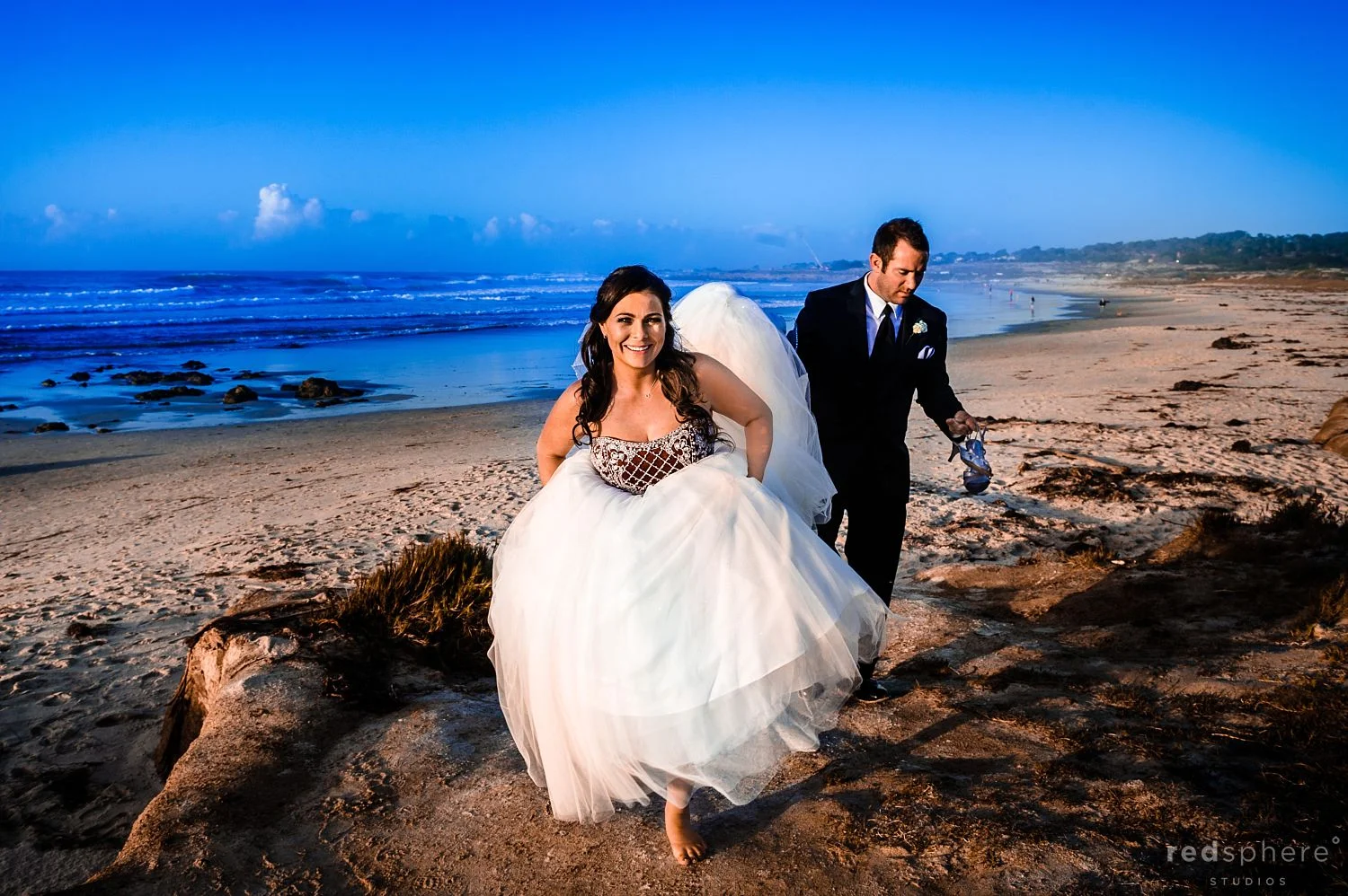 Groom Holds The Brides Heels as They Roam Pebble Beach, California, Sunny Day