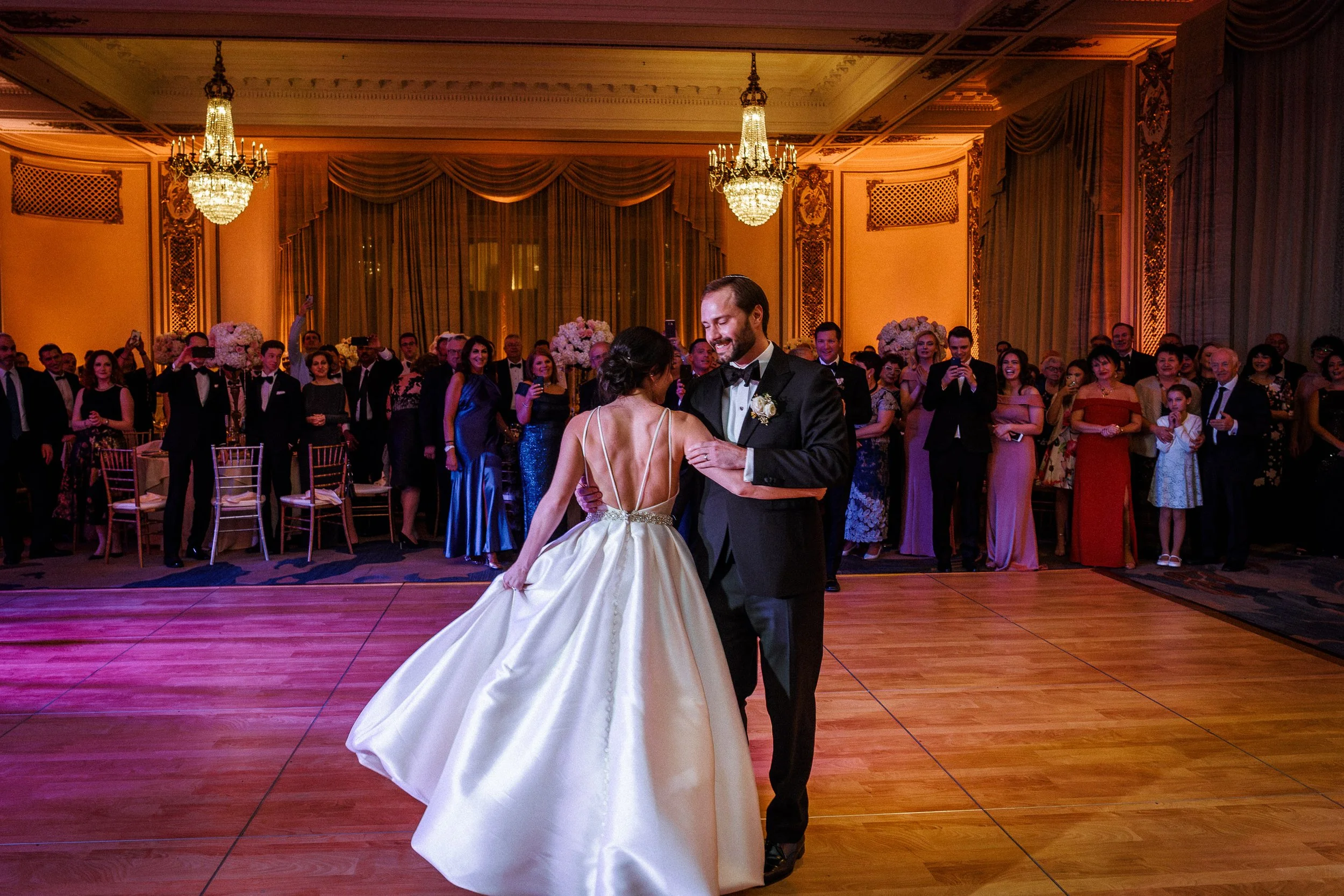 A bride and groom sharing their first dance at a wedding reception in an elegant ballroom, surrounded by guests.
